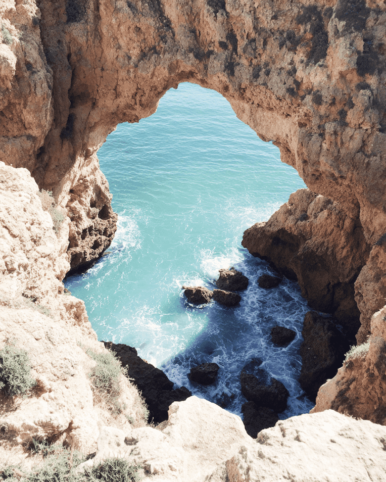 Elegant seaside restaurant with wooden tables and ocean view through arched doors.