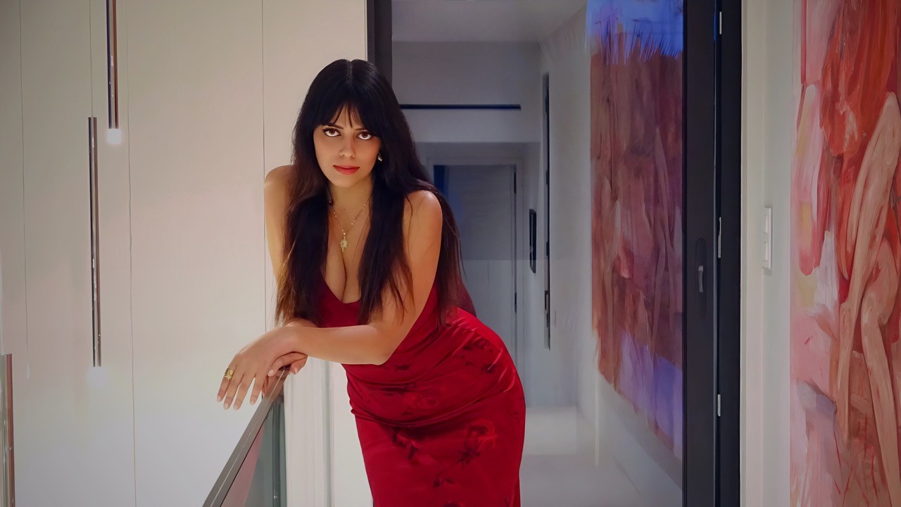 A young person with long, wavy hair sits in front of a plain background, looking directly at the camera.