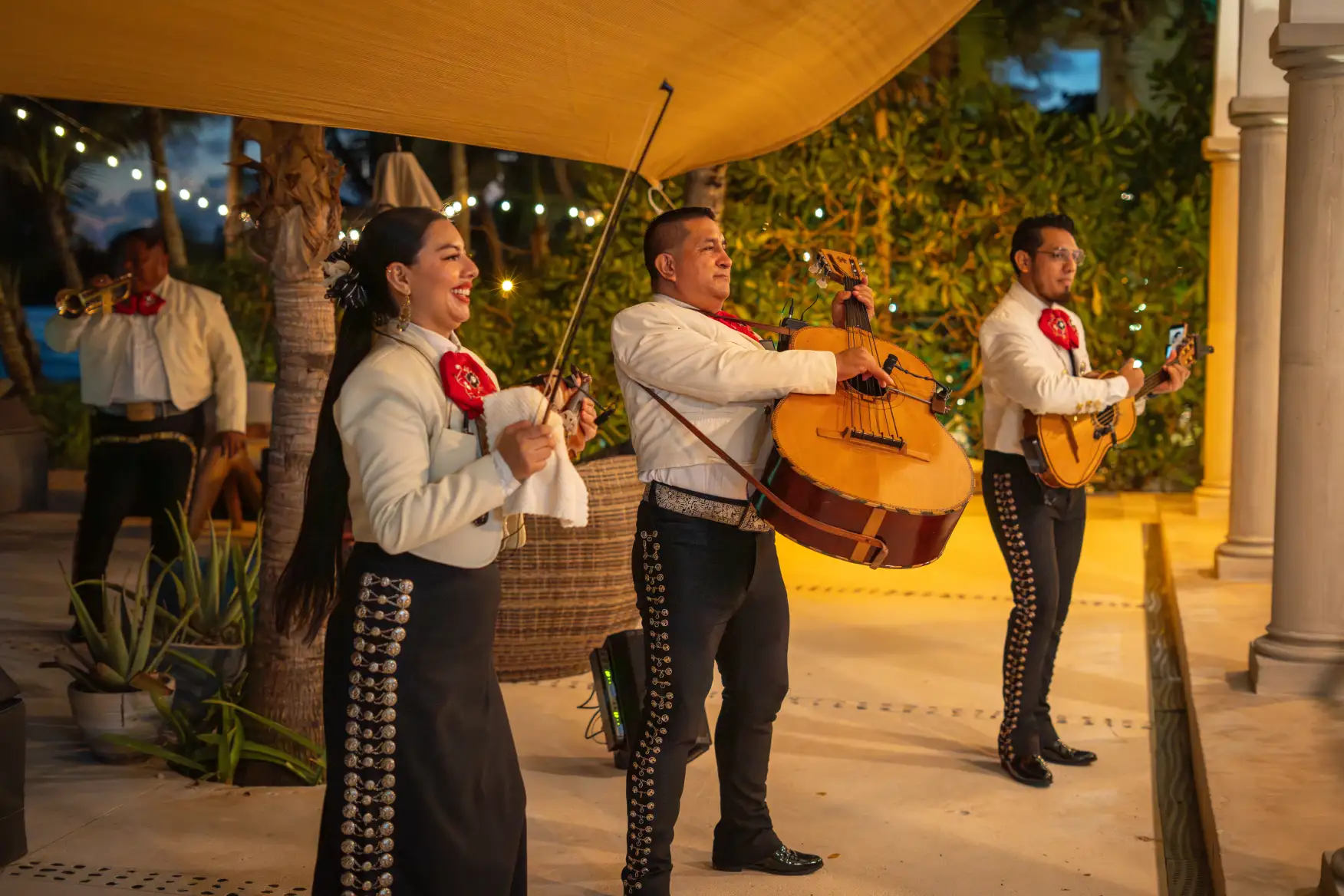Smiling mariachi band performing with violin, guitars, and trumpet.