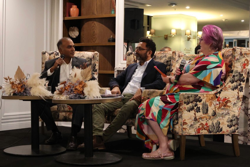 three speakers look at one another, one holds a microphone