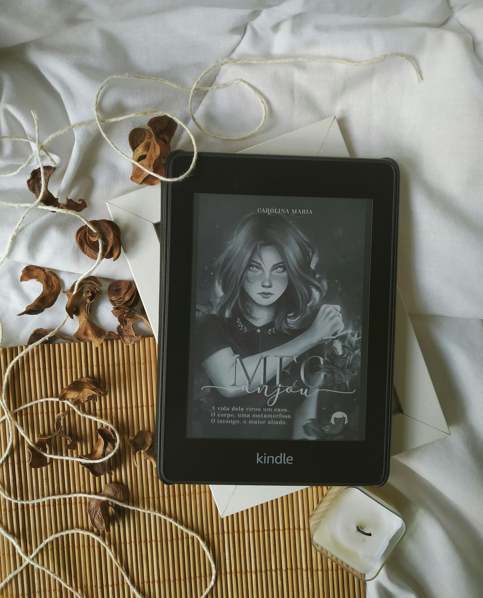 A black Kindle e-reader displaying a cover of a book, surrounded by white fabric and dried leaves.