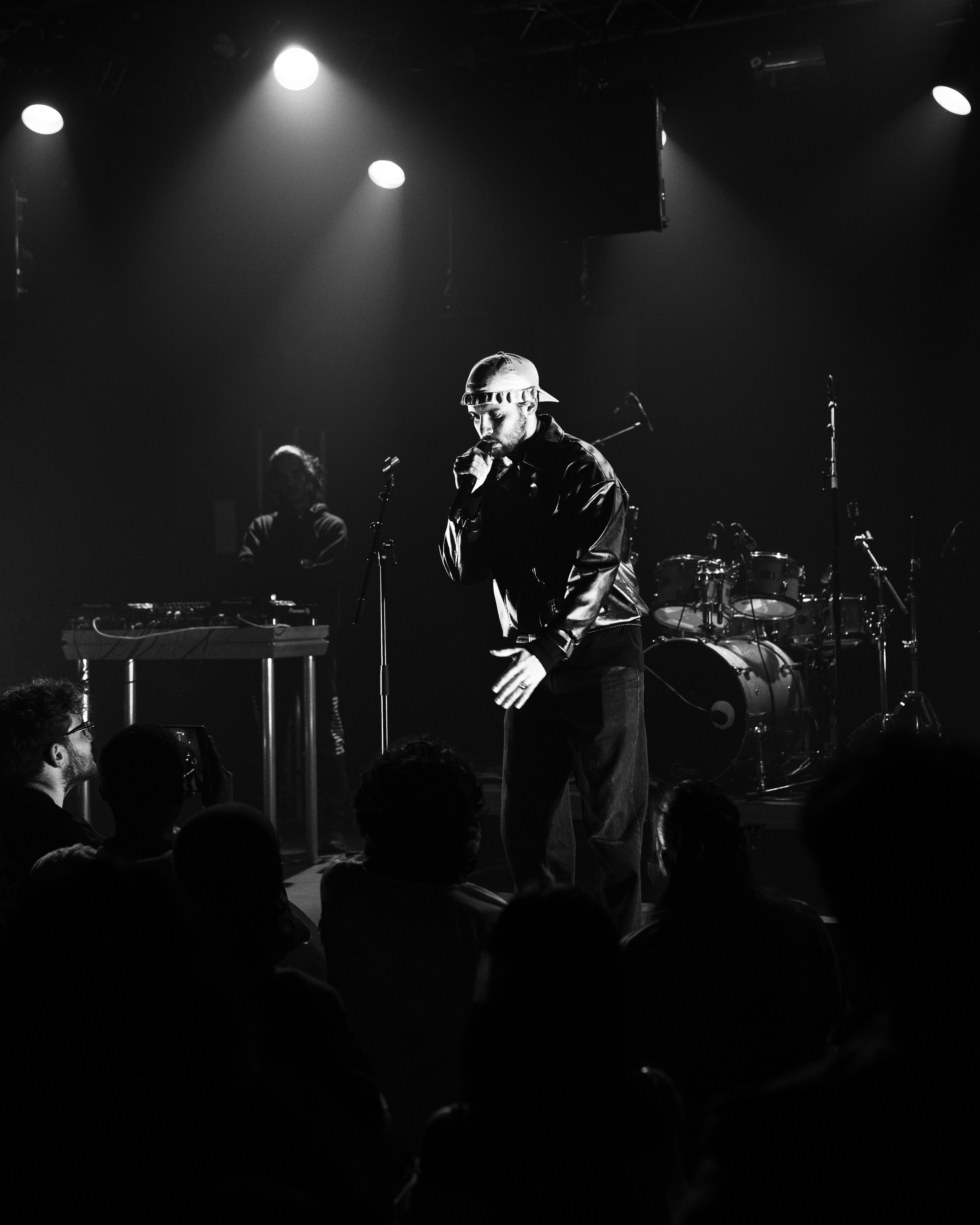 A close-up shot of a woman with long dark hair blowing across her face, revealing one eye. She wears a white shirt with a single yellow flower tucked in, set against a blue sky.