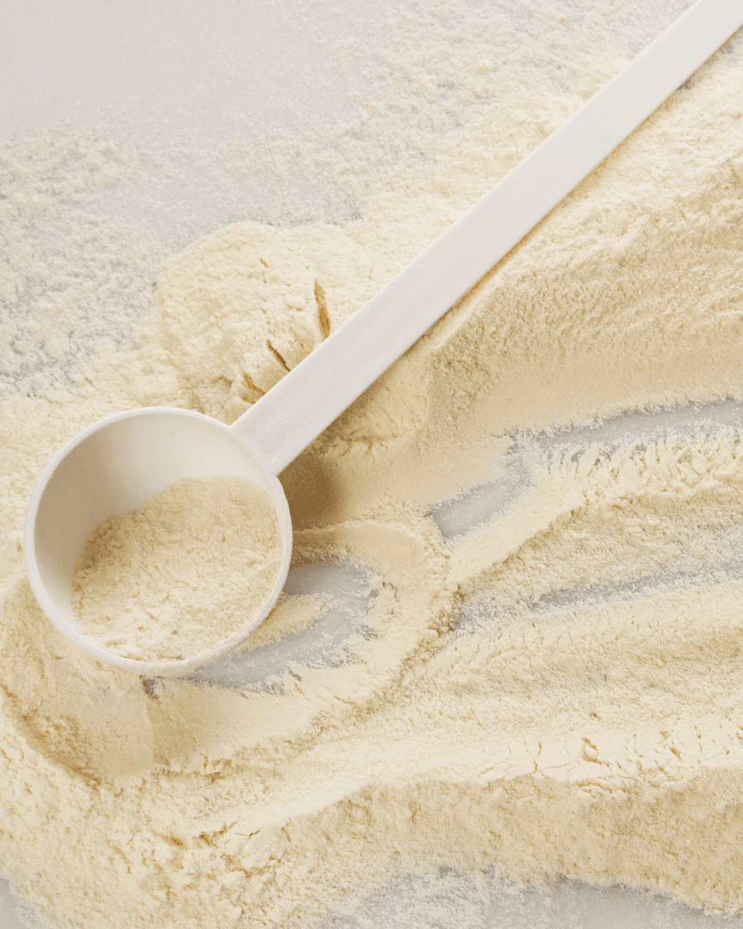 White protein powder spread on a surface with a small white scoop.