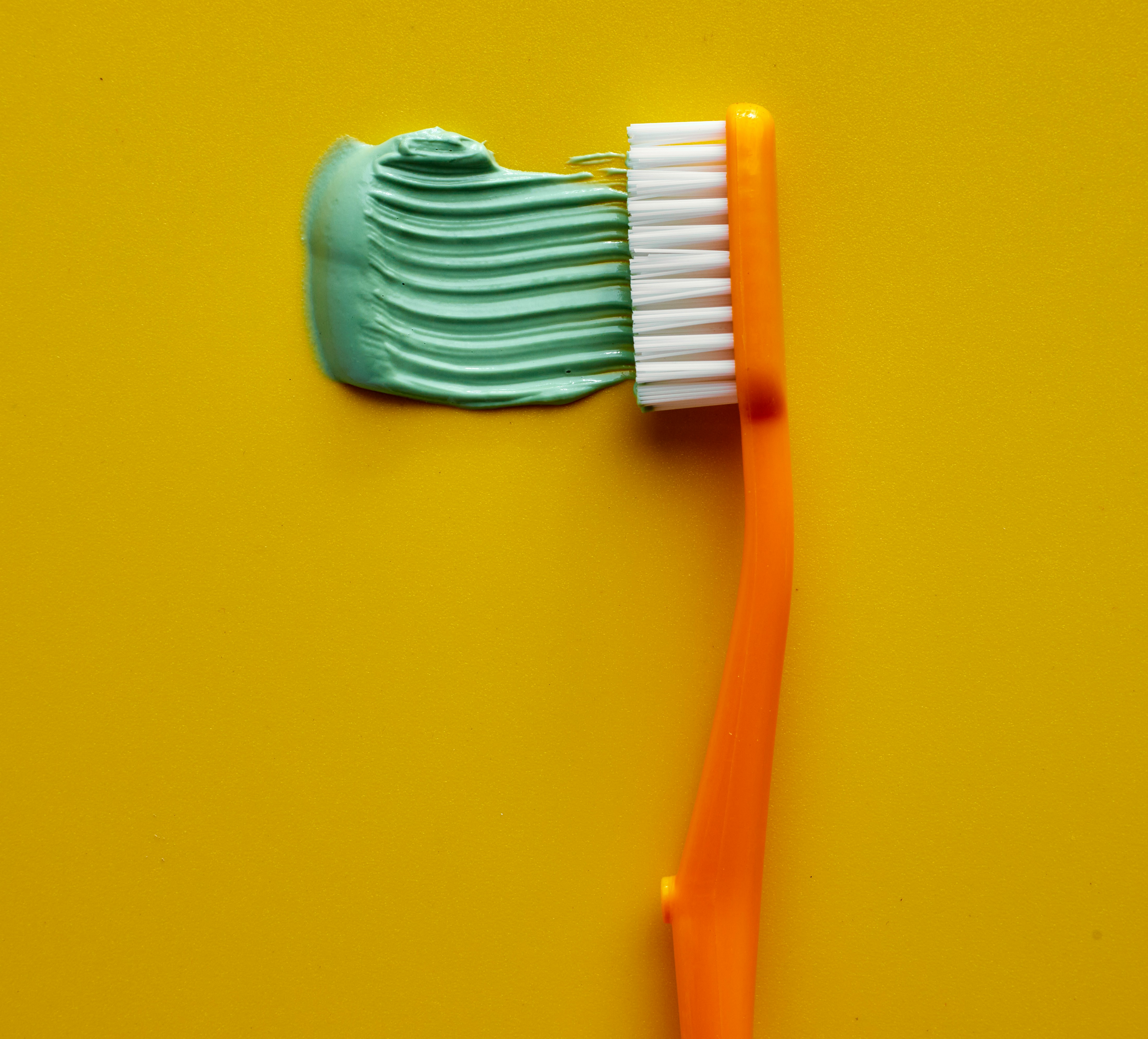 Orange toothbrush with green toothpaste on yellow background