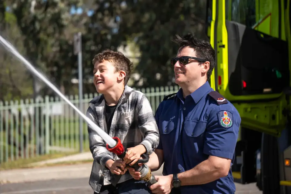 Firefighter and child holding a water hose together