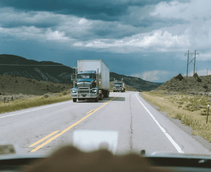 Semi-trucks driving on a rural highway under cloudy skies, viewed from a vehicle