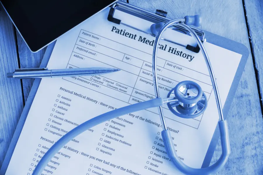 Medical scribe documentation represented by a patient medical history form on a clipboard with a stethoscope and pen.