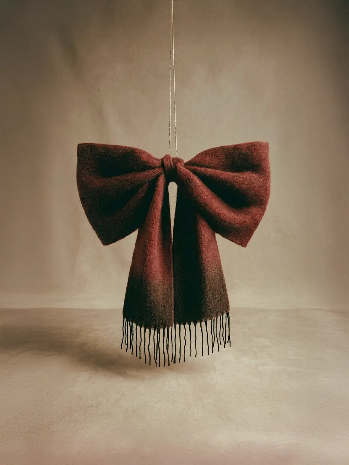 A large, elegant burgundy bow with fringe detailing hangs against a minimalist, beige backdrop, showcasing high-end fashion brand aesthetics in this AI production project visual.