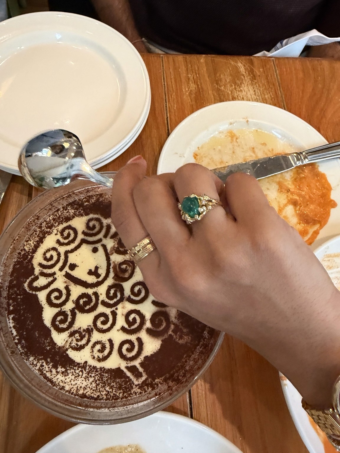 An emerald ring, a hand, and a patterned dessert. Photograph by Pranjali Shah.