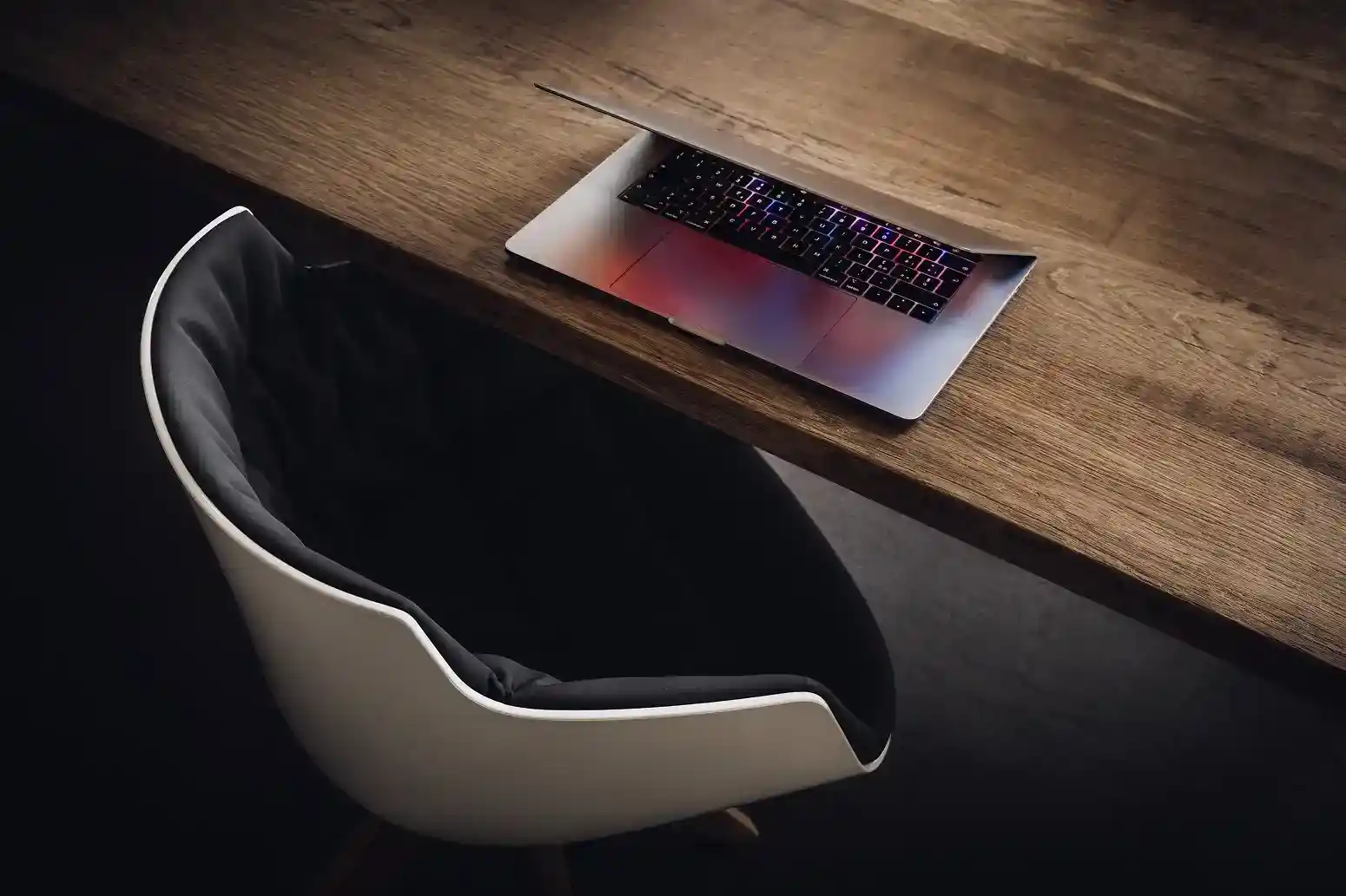 Open laptop on a wooden desk beside an empty chair.