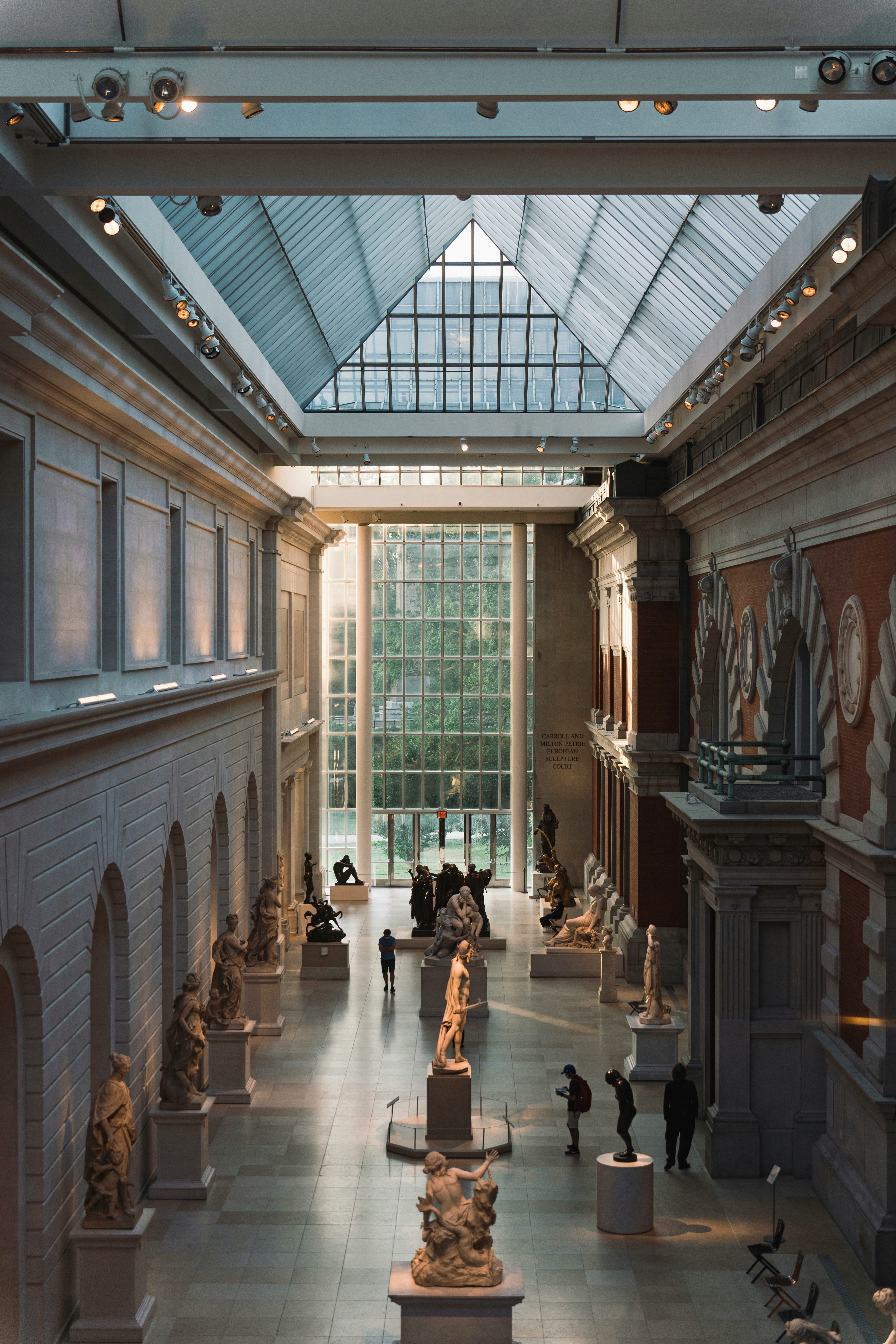 A hall lined with statues looking towards a glass wall within the Metropolitan Museum of Art in New York City.