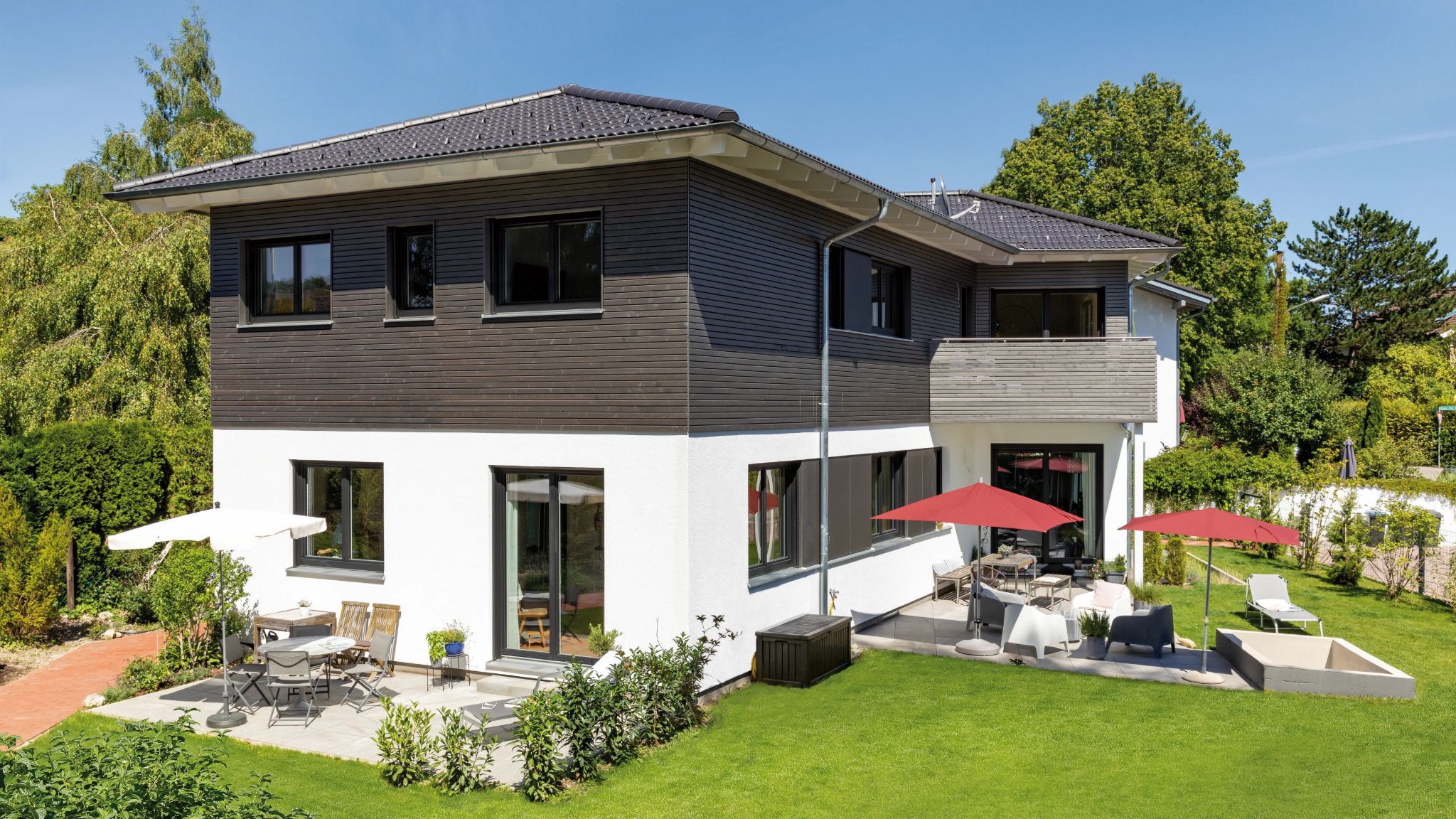 Modernes zweistöckiges Haus mit Hol Fassade und weißen Putz, mit Terrasse, Gartenmöbeln und roten Sonnenschirmen