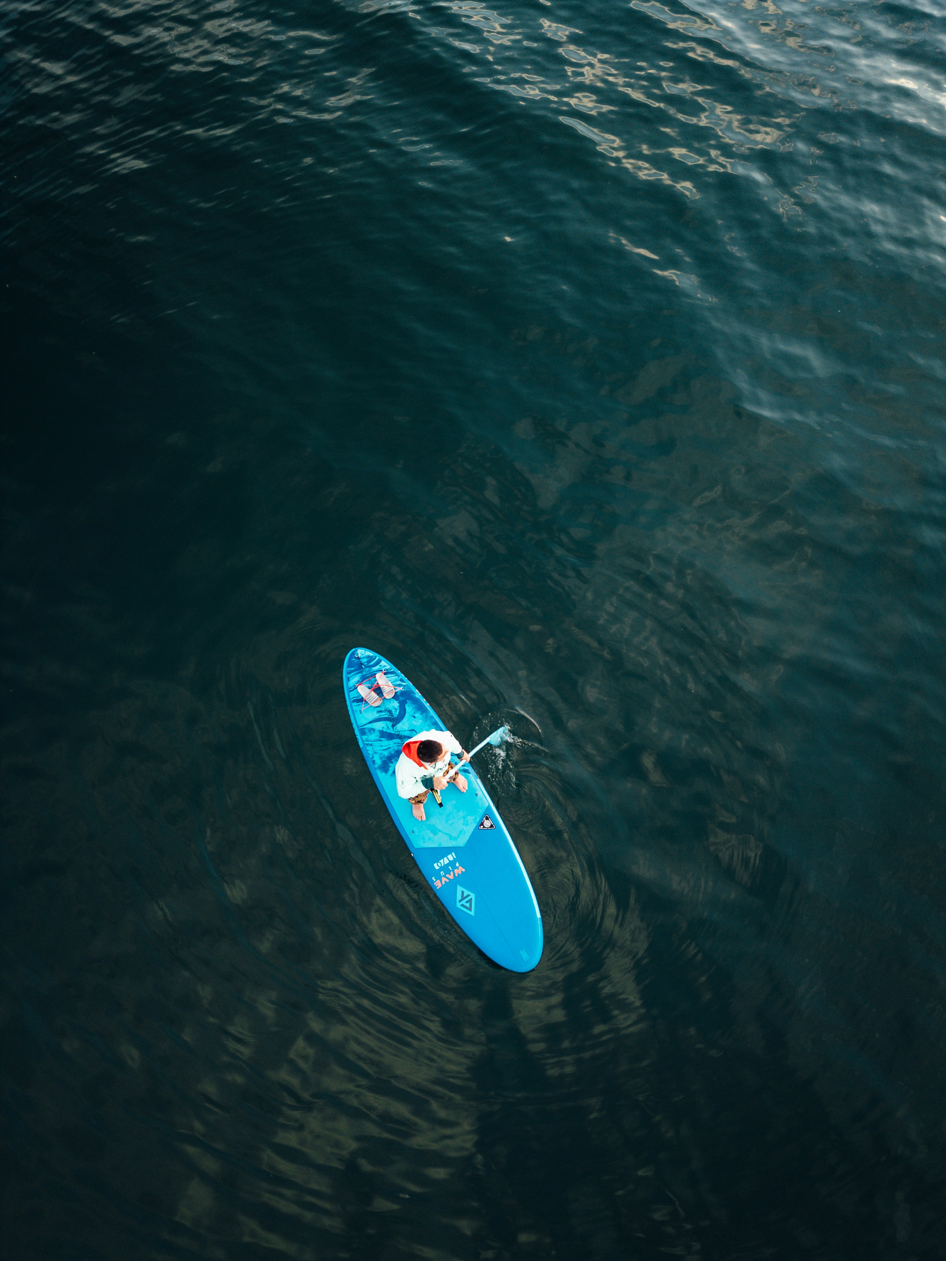 A person paddleboarding on a dark blue ocean.