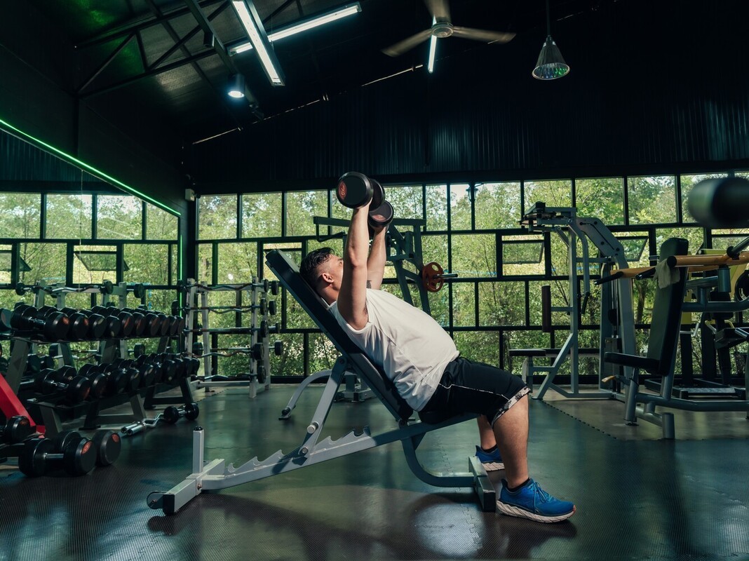 overweight man using dumbbells on a bench for weight lifting for weight loss at the gym