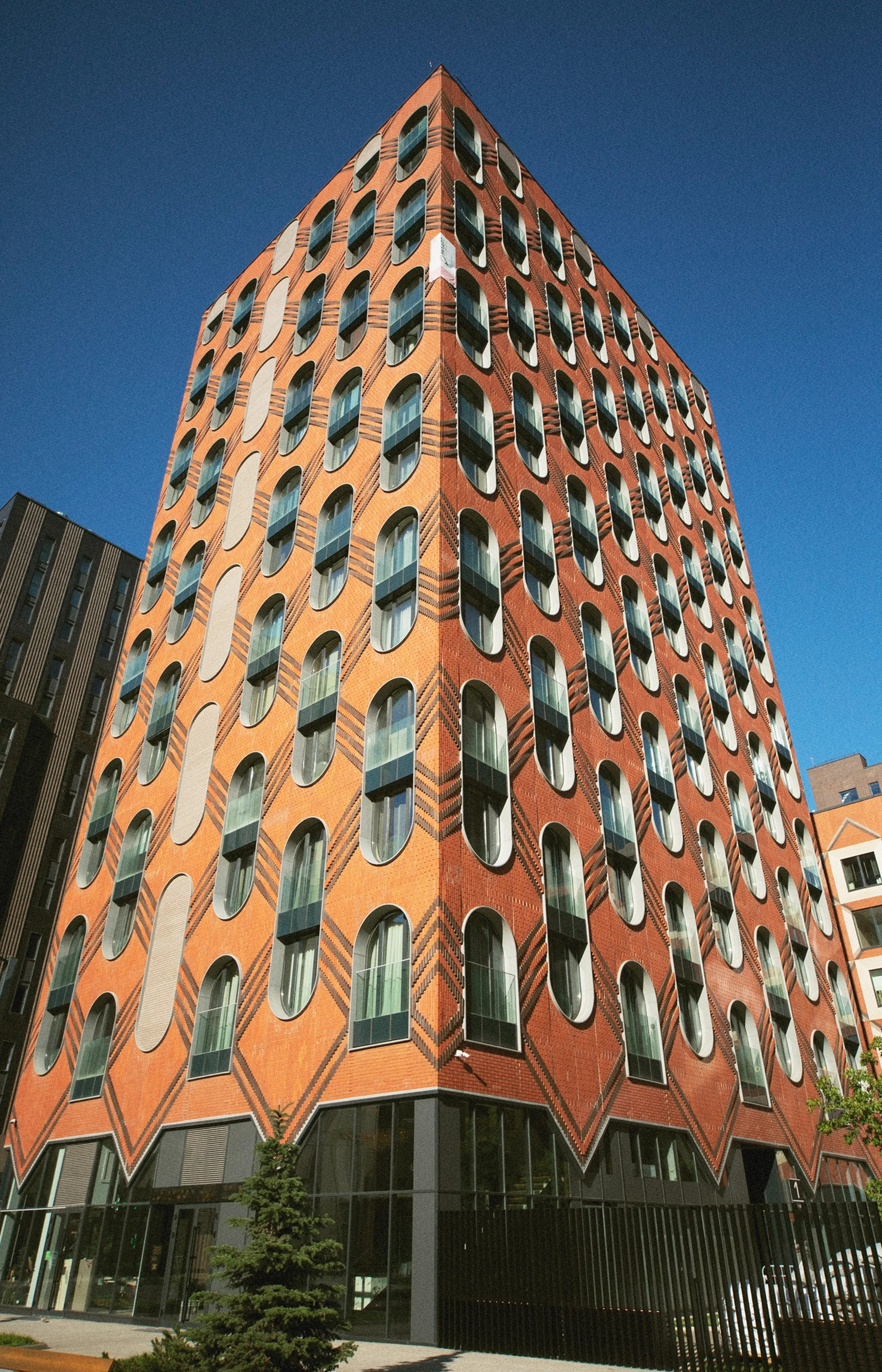 High-rise building facade with orange walls and repeating oval windows arranged in a rhythmic vertical pattern.