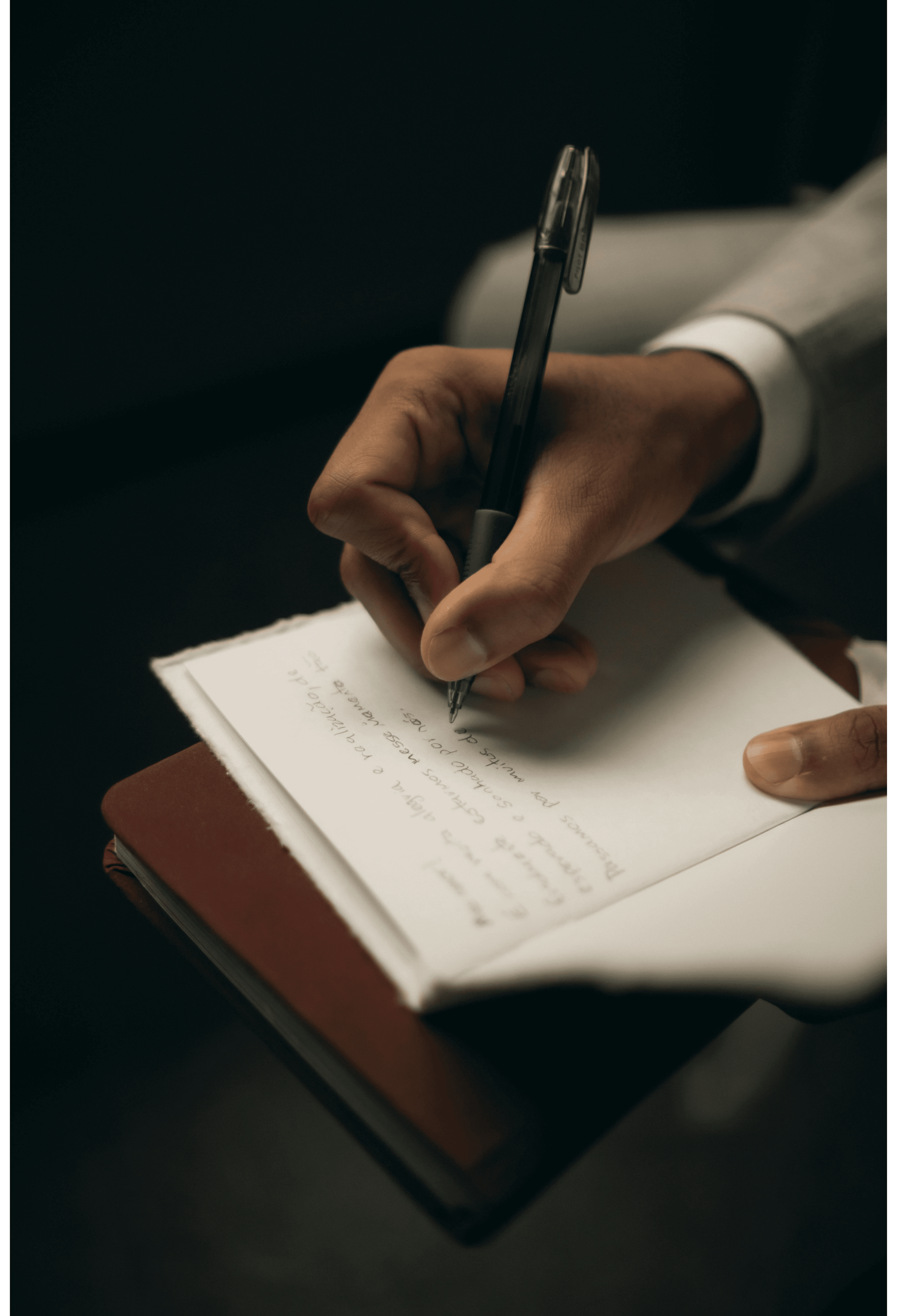 Close up of hands writing in leather notebook on wooden desk