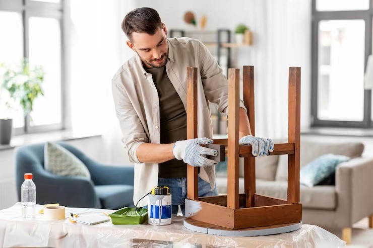 Man fixing a wooden chair while wearing gloves. DIY furniture repair and restoration. Interior repair.