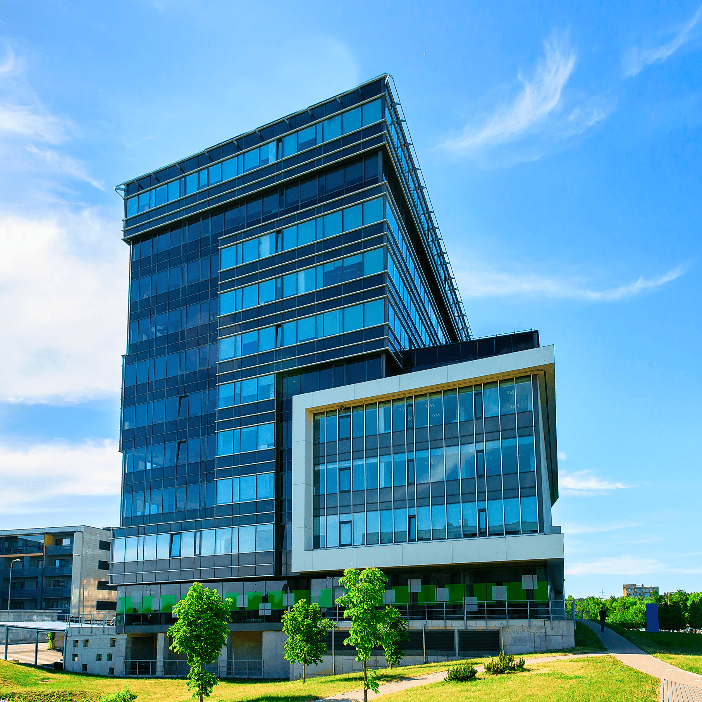 Modern glass office building with white framing, lawn, trees, and clear sky