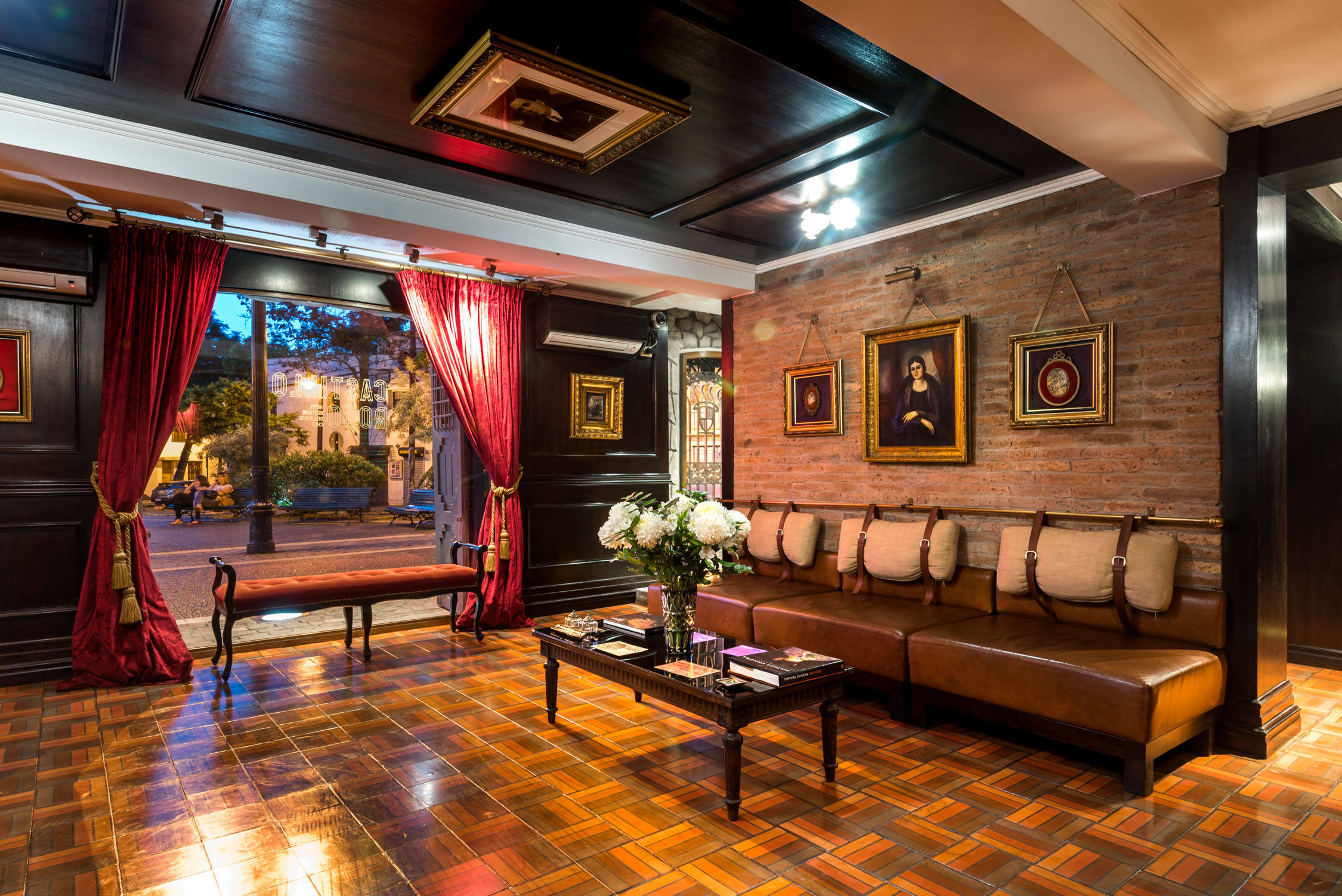A cozy lounge with leather sofas, a brick wall, framed paintings, and a large painting of a landscape in a frame.
