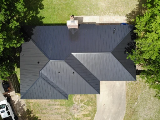 Finished black standing-seam roof with intersecting hips, valleys and a red-brick chimney.