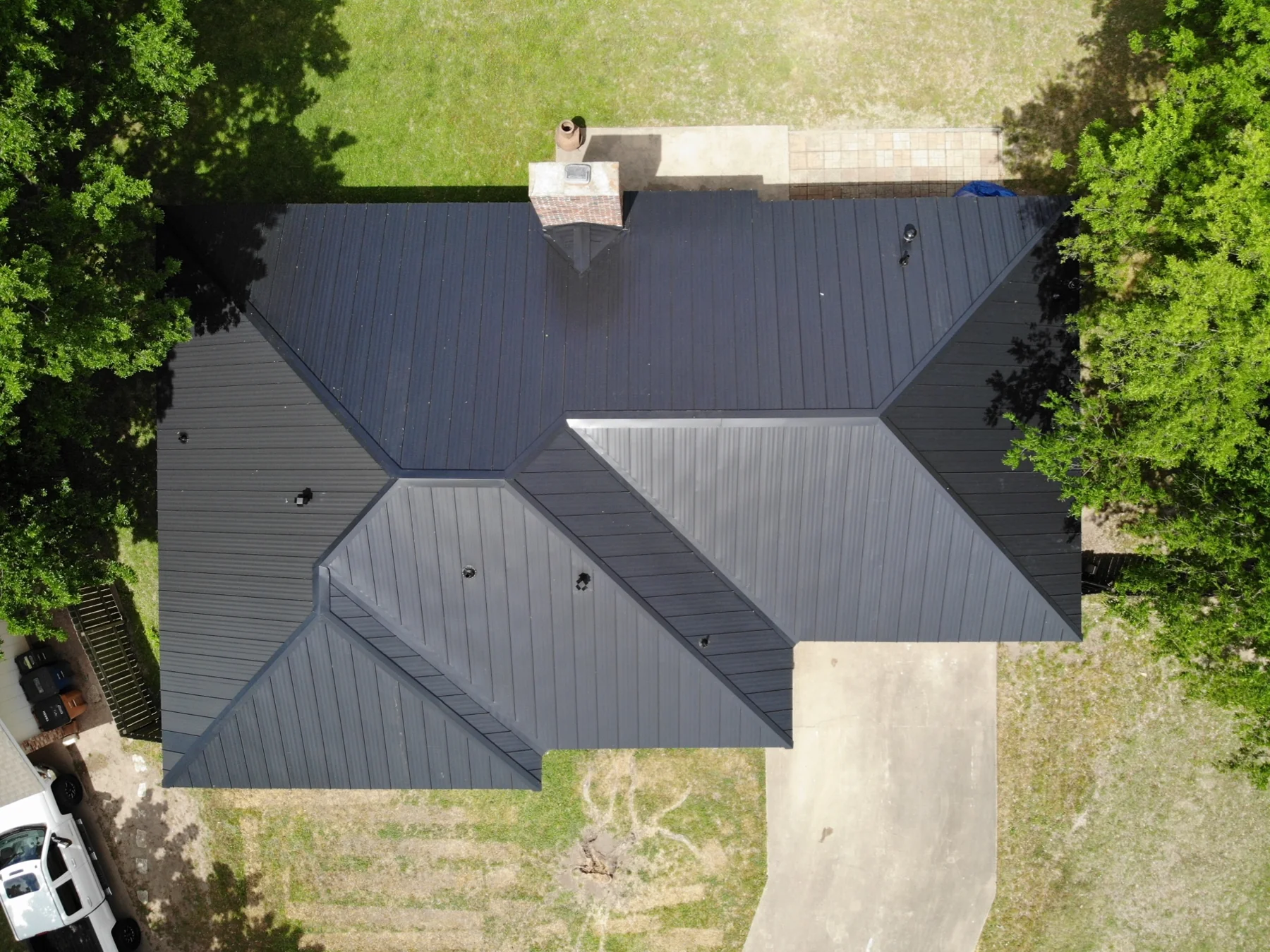 Finished black standing-seam roof with intersecting hips, valleys and a red-brick chimney.
