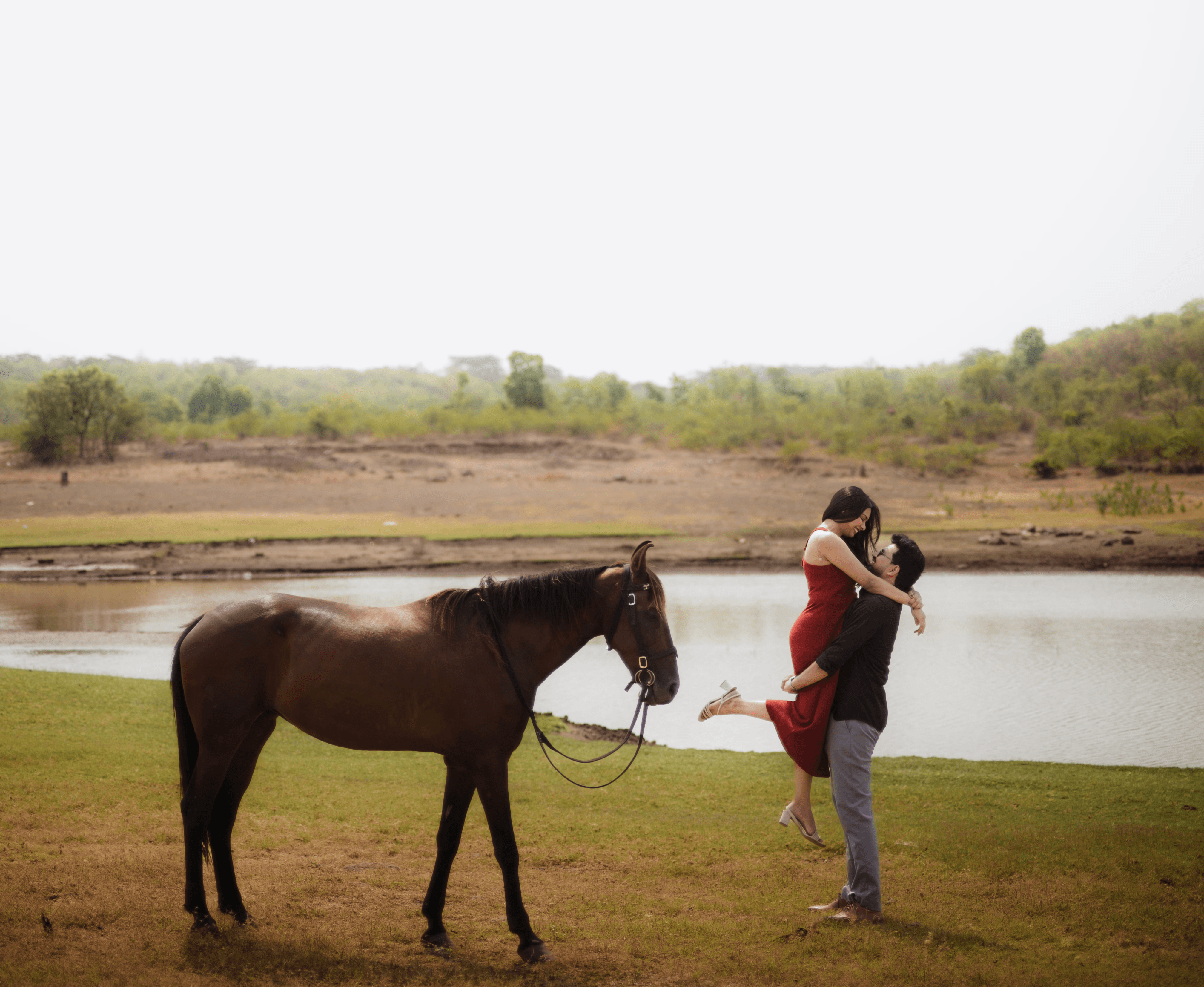 A couple posing beside a lake with a horse included.