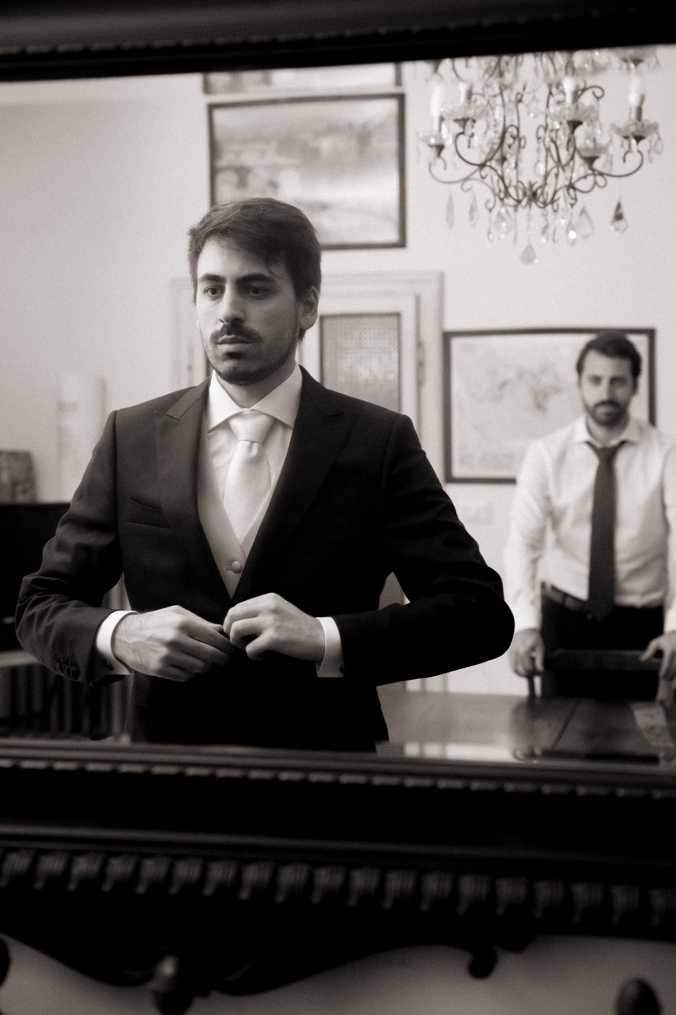 Matteo si aggiusta la cravatta prima della cerimonia, ritratto in bianco e nero negli interni eleganti di Villa Peroni Riva