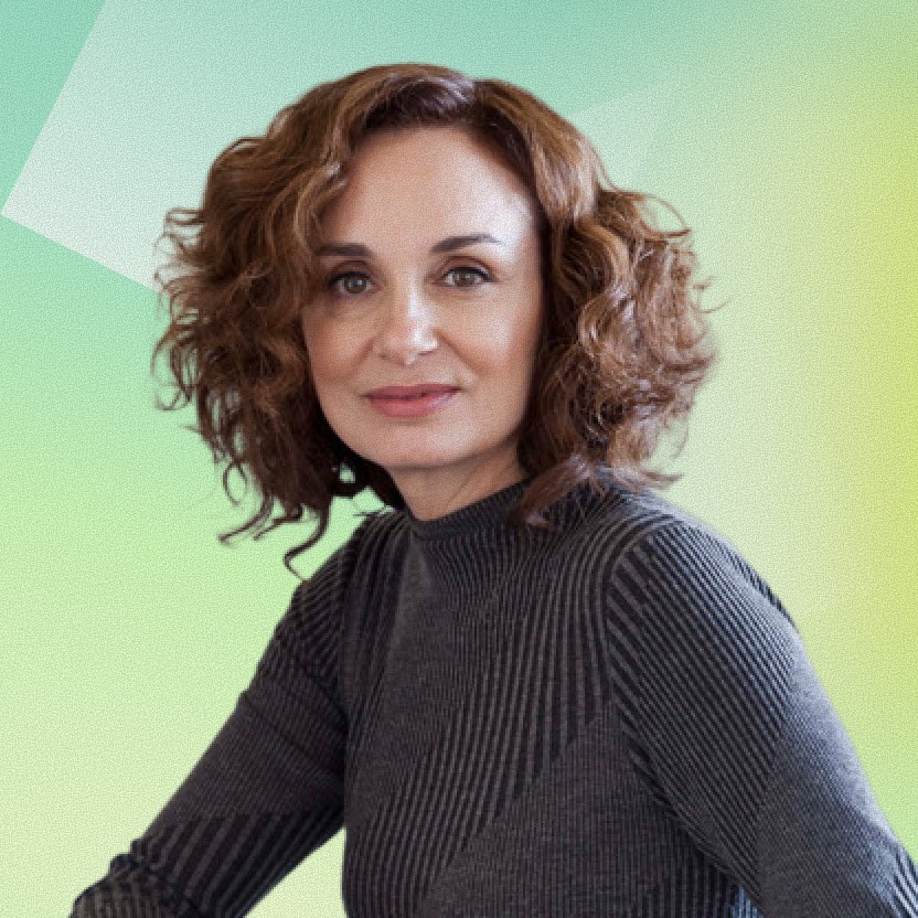 Close-up portrait of a freckled woman with soft pink hair and star earring, natural light, white tank top.