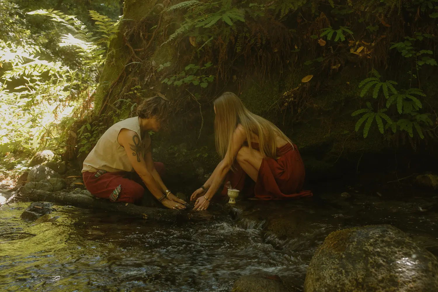 Man and woman touching water in jungle stream during earth-based ceremony