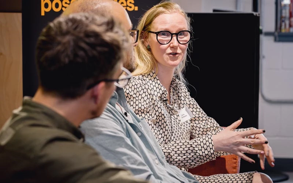 Speakers engage in conversation during a live panel discussion. The relaxed seating and close interaction emphasise dialogue and collaboration.