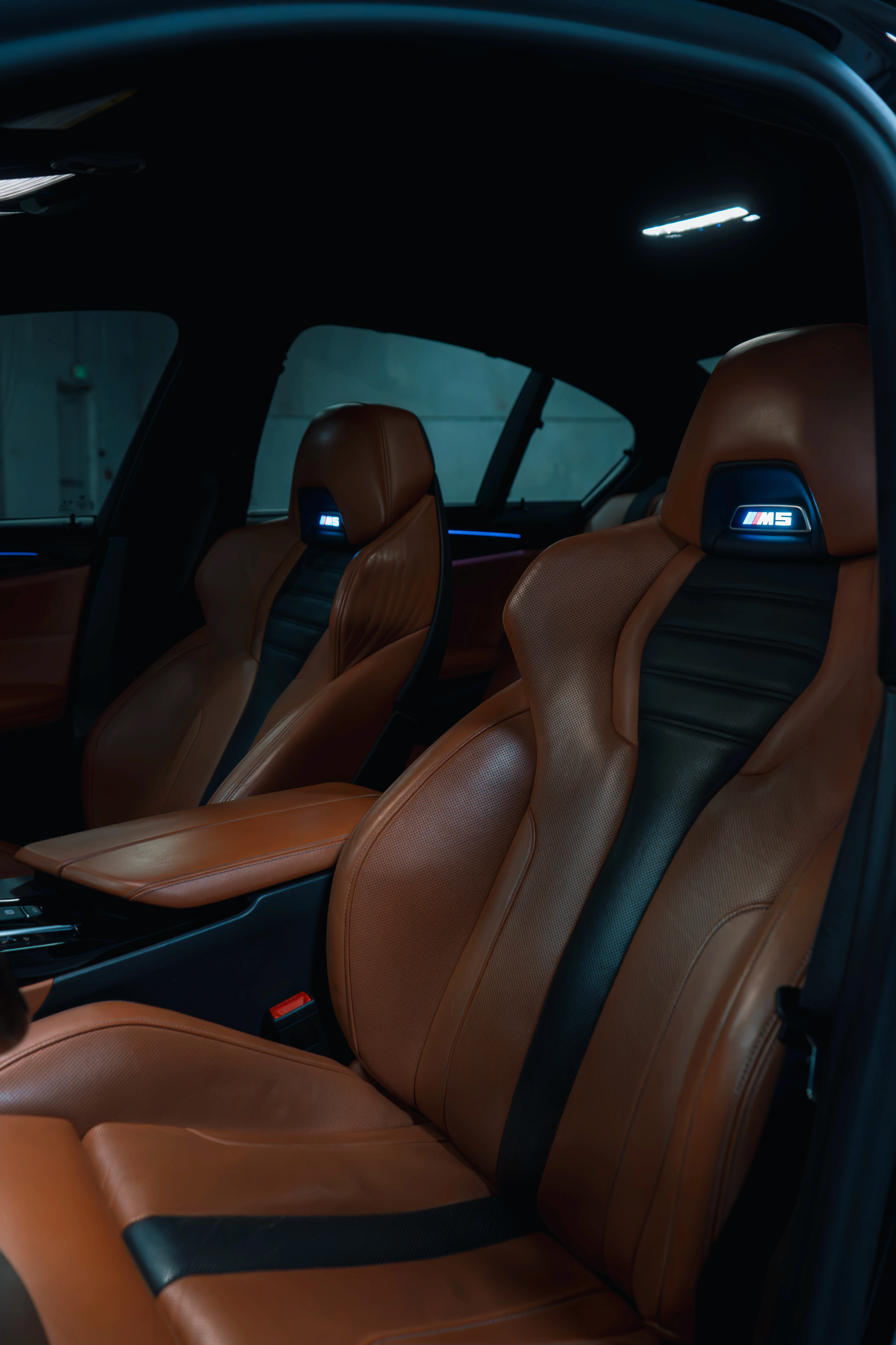 Two people in a workshop, one standing and smiling while the other leans over a car, working on it.
