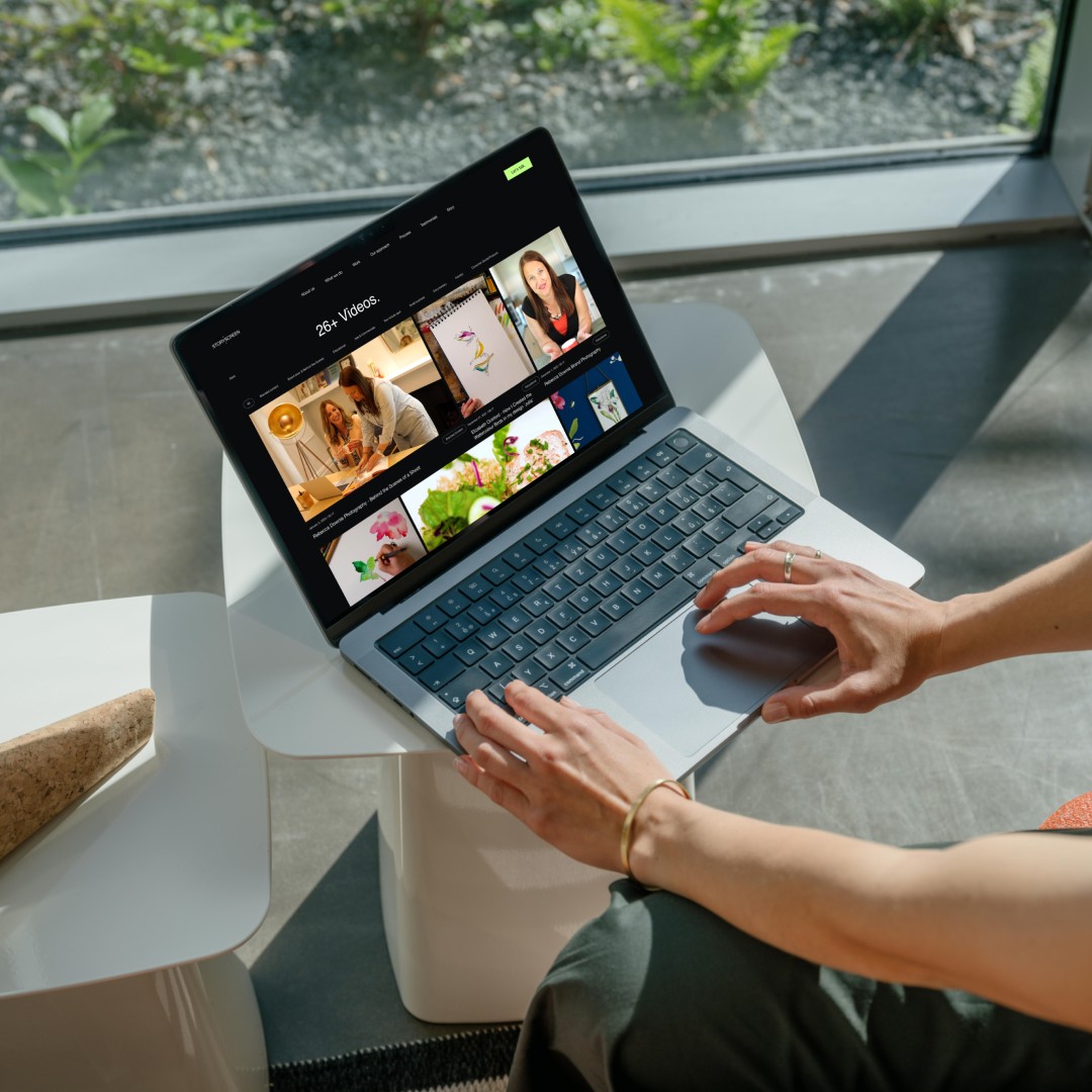 Modern home office setup with a monitor, ergonomic chair, keyboard, and indoor plants near a window with blinds.