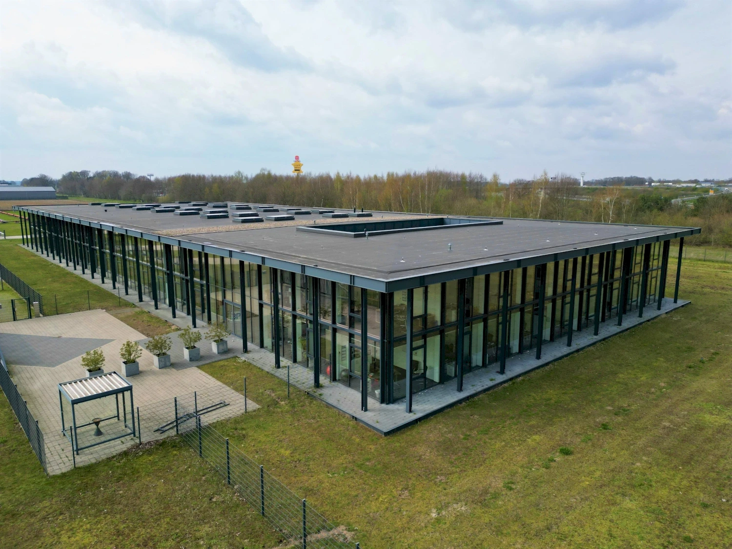 Modern headquarter office building with large windows and a flat roof, surrounded by grass and trees under a cloudy sky.