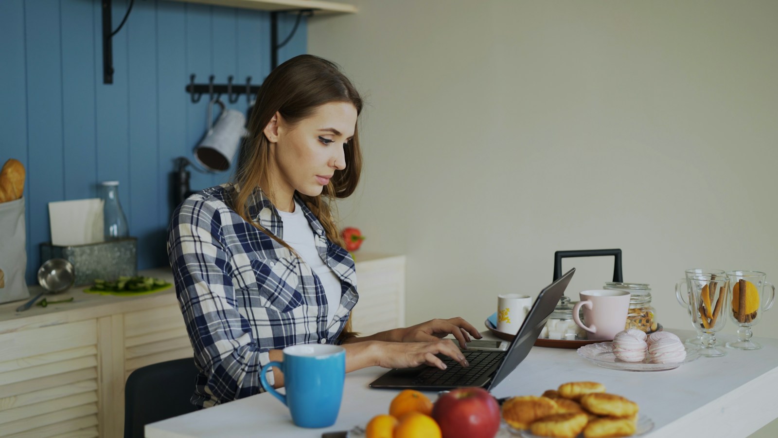 A woman using her laptop at a bright kitchen table to connect with her dietitian online, with fruit and coffee nearby