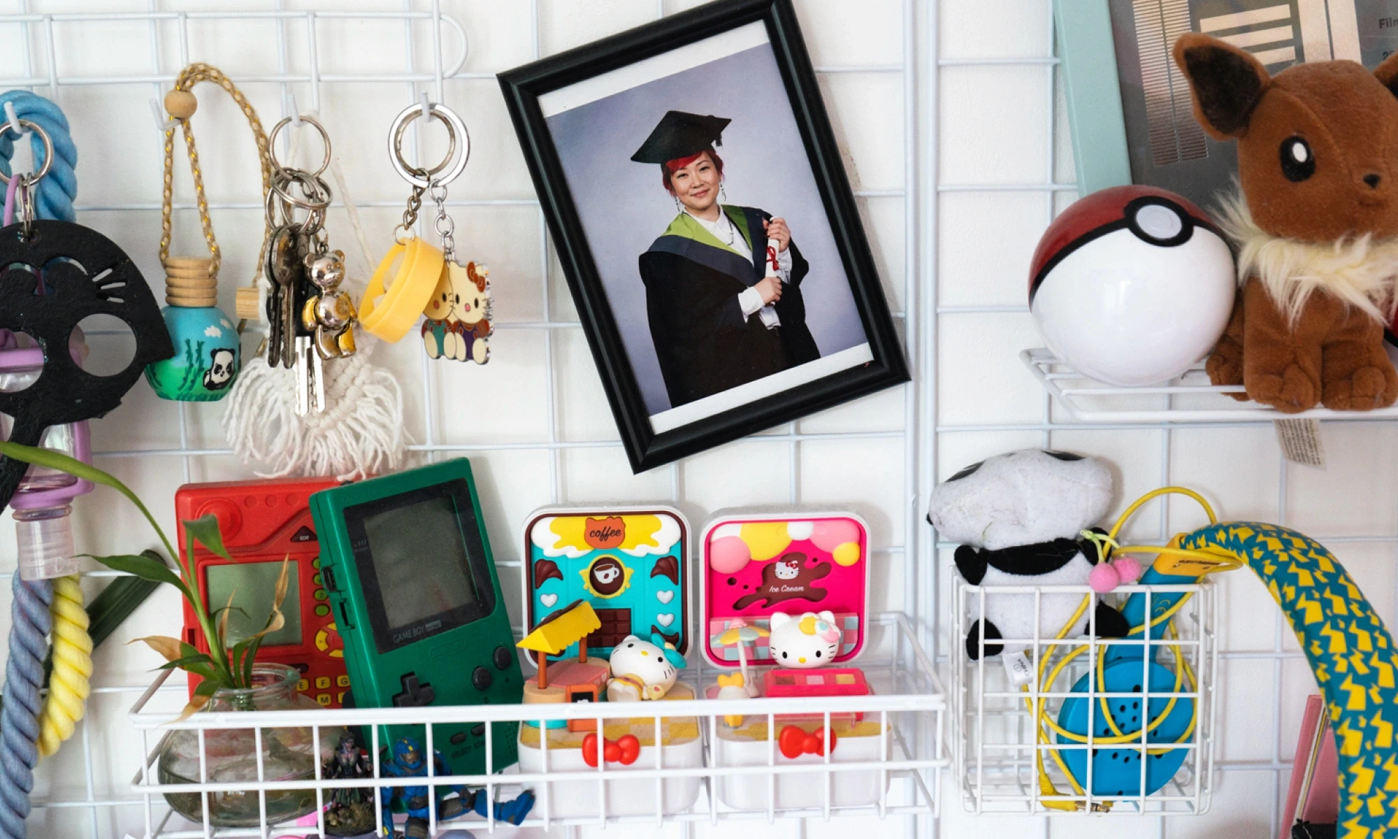 Woman in graduation gown surrounded by various trinkets such as Pokémon, Game Boy, and key rings