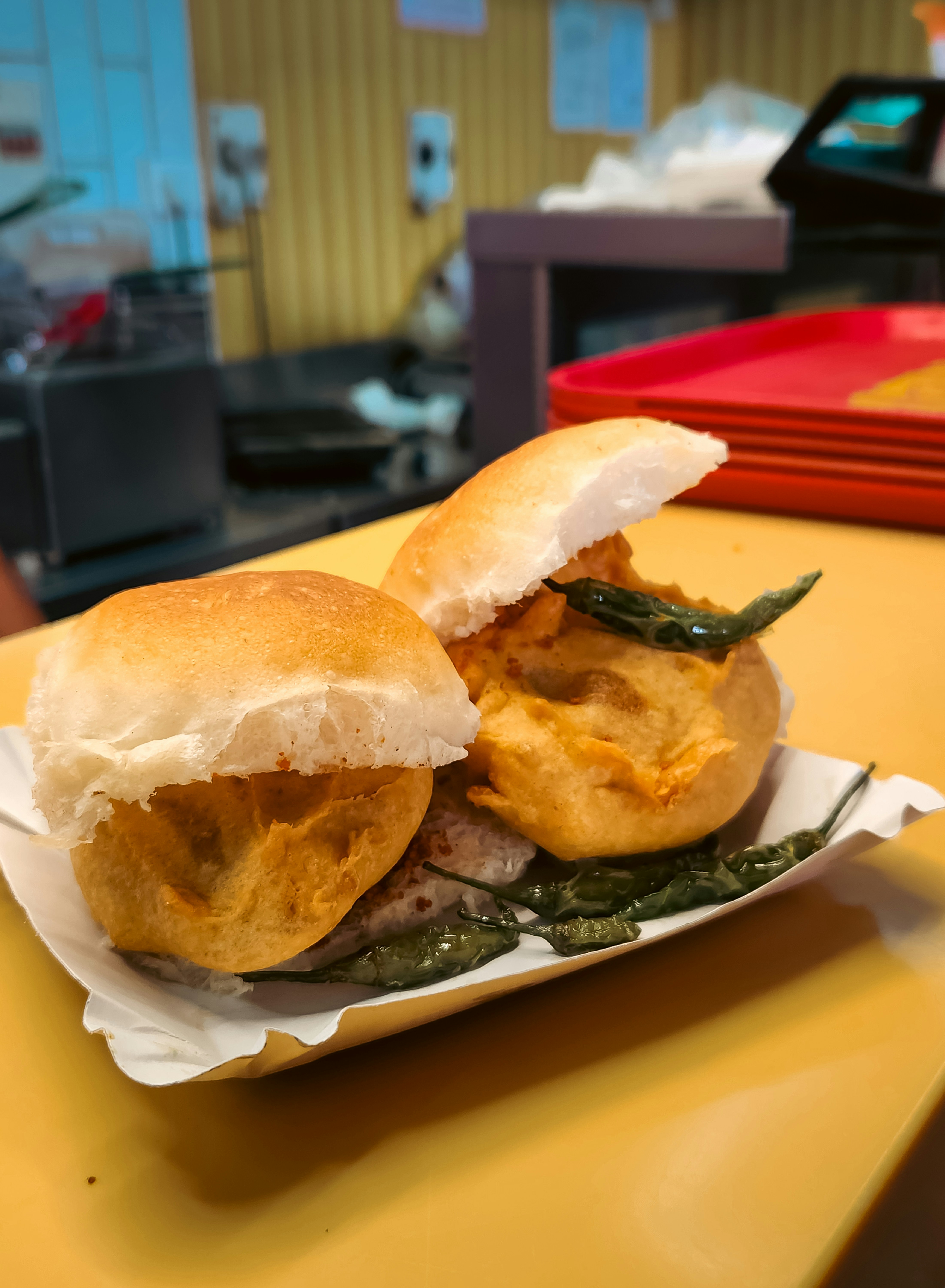 Two vada pav sandwiches on a paper plate.