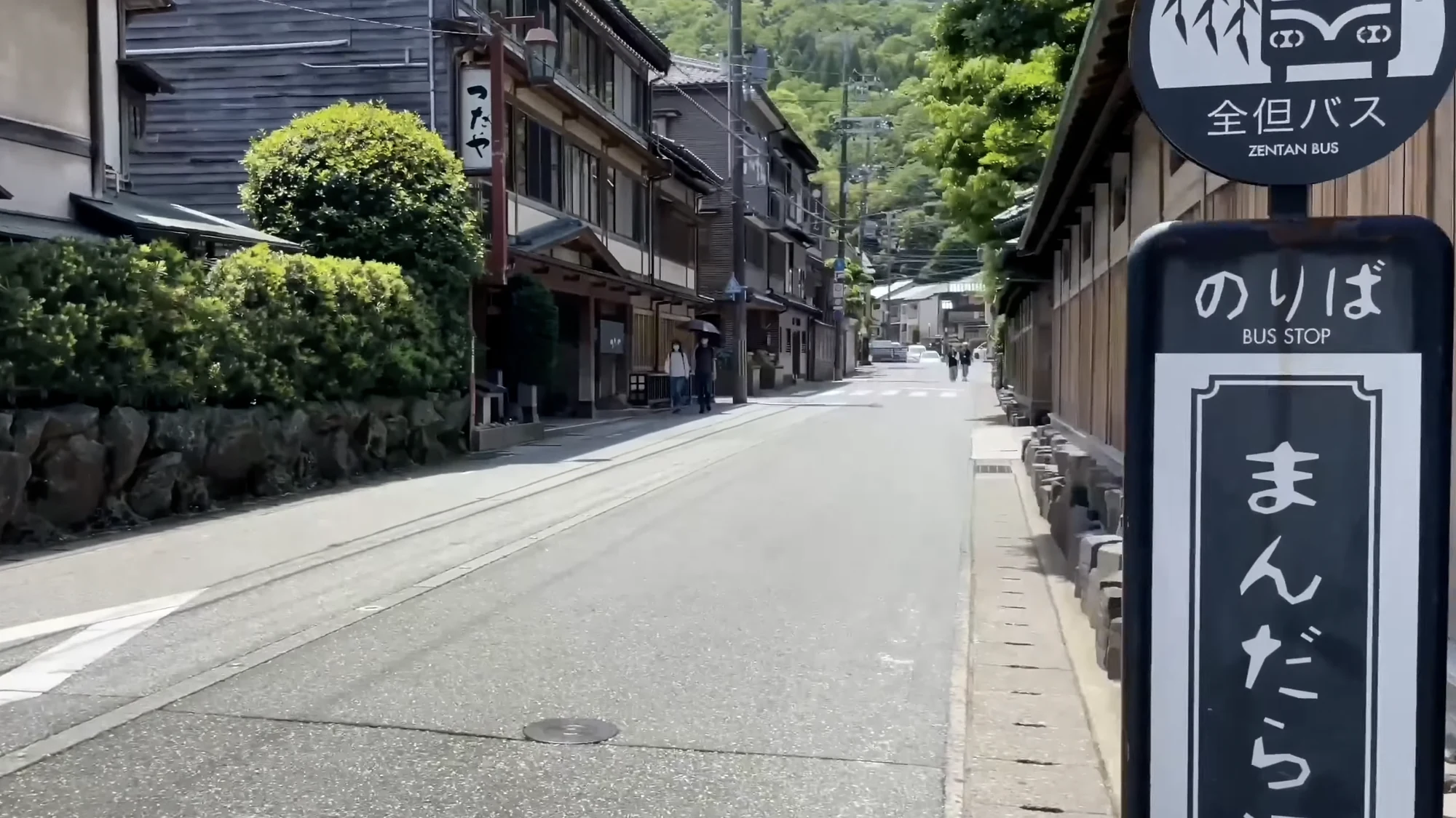 A Zentan Bus stop sign in Kinosaki reading Mandara-yu with the bathhouse behind it.