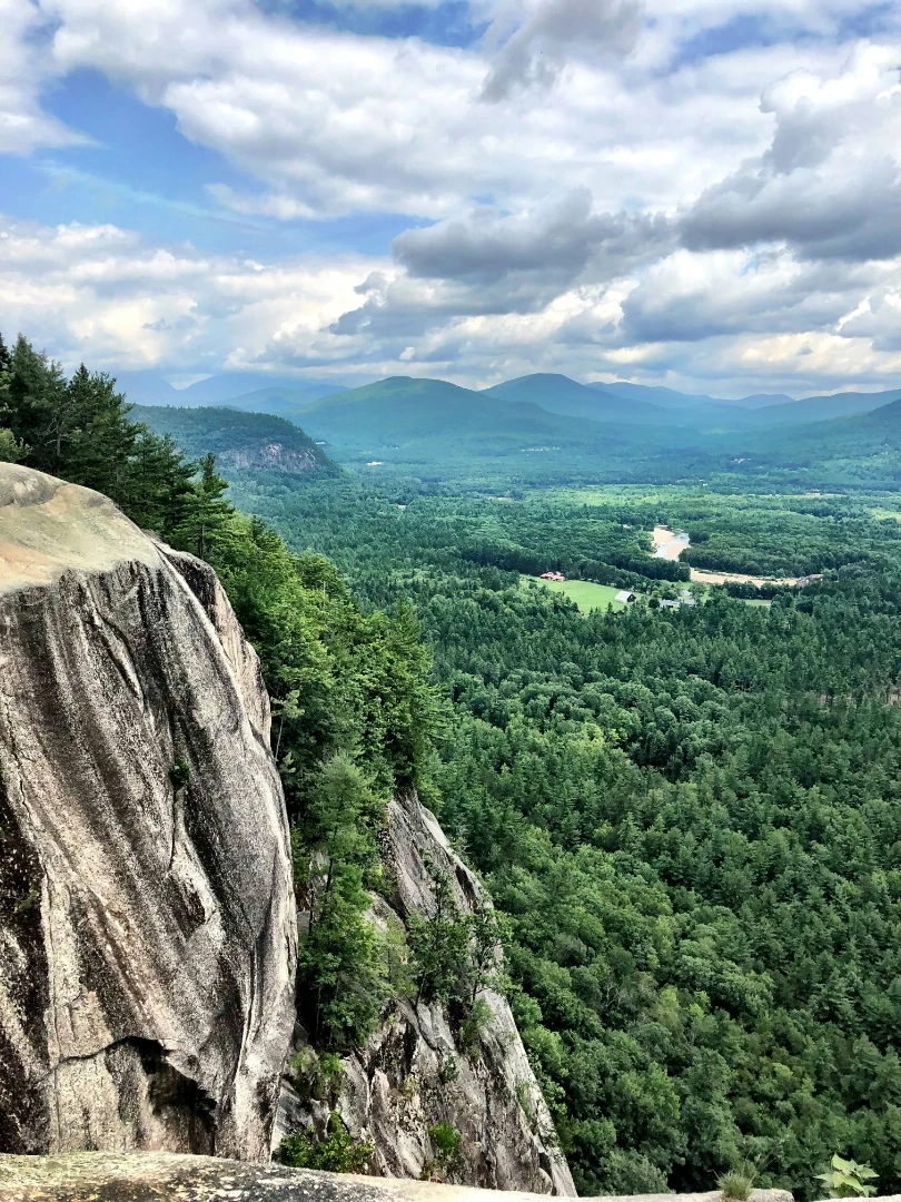 Daytime shot of Cathedral Ledge overlooking green trees on mountain in the distance.