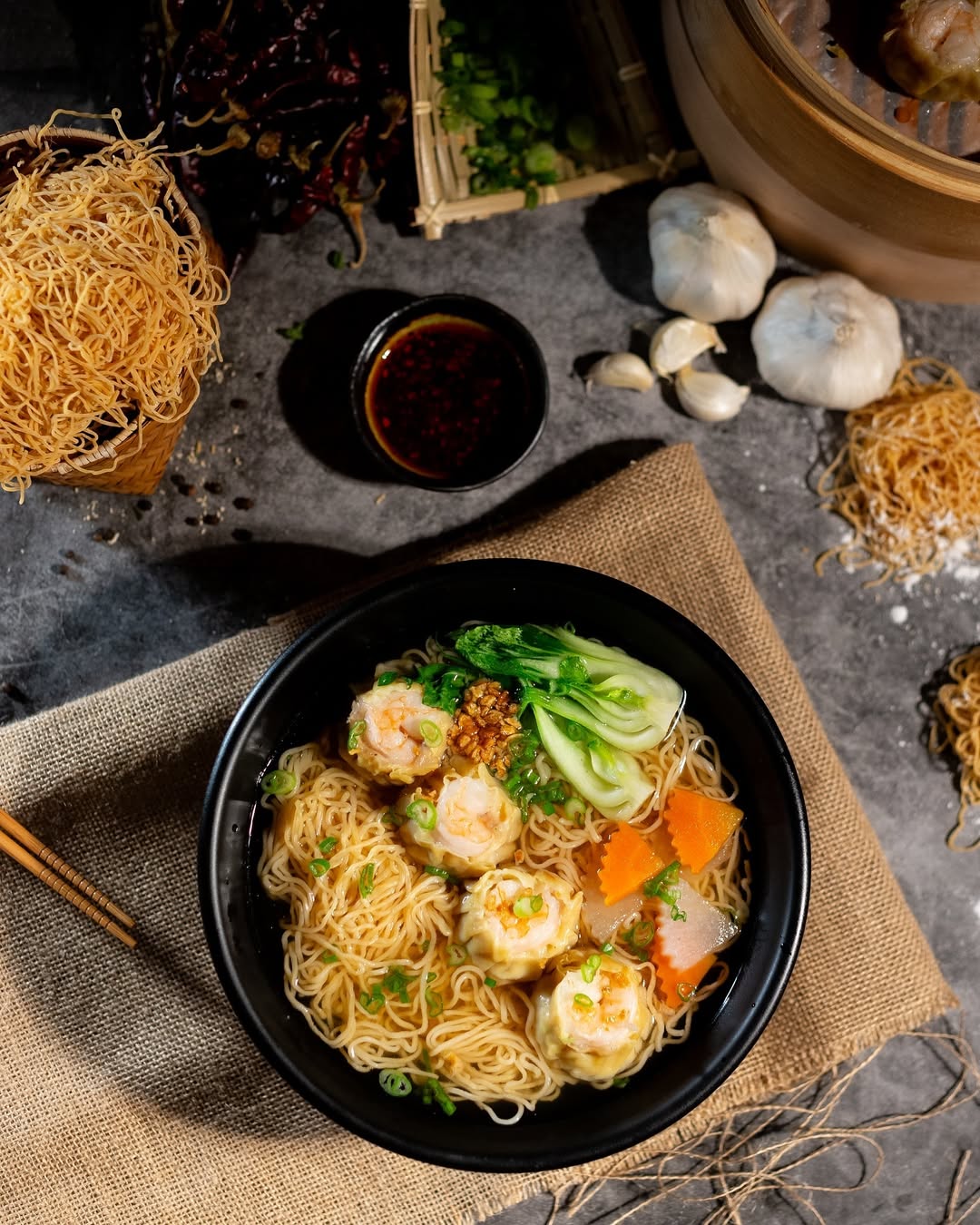 A vibrant bowl of spicy noodle soup, topped with fresh herbs, sliced chili peppers, and tender meat, showcasing Dumpling n Dips’ signature Sichuan flavors.