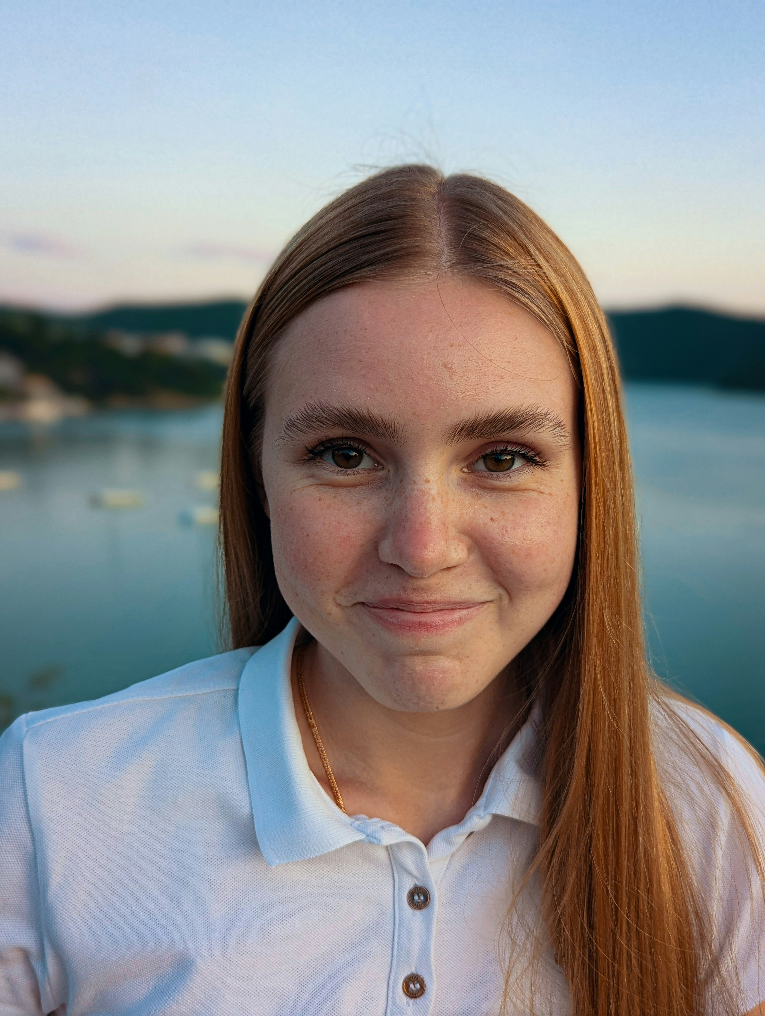 A woman smiles at the camera, outside near water.