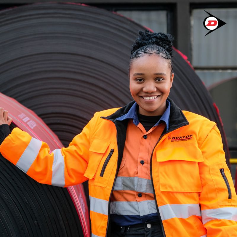 Smiling young man with short hair poses against a dark background, wearing a green button-up shirt.