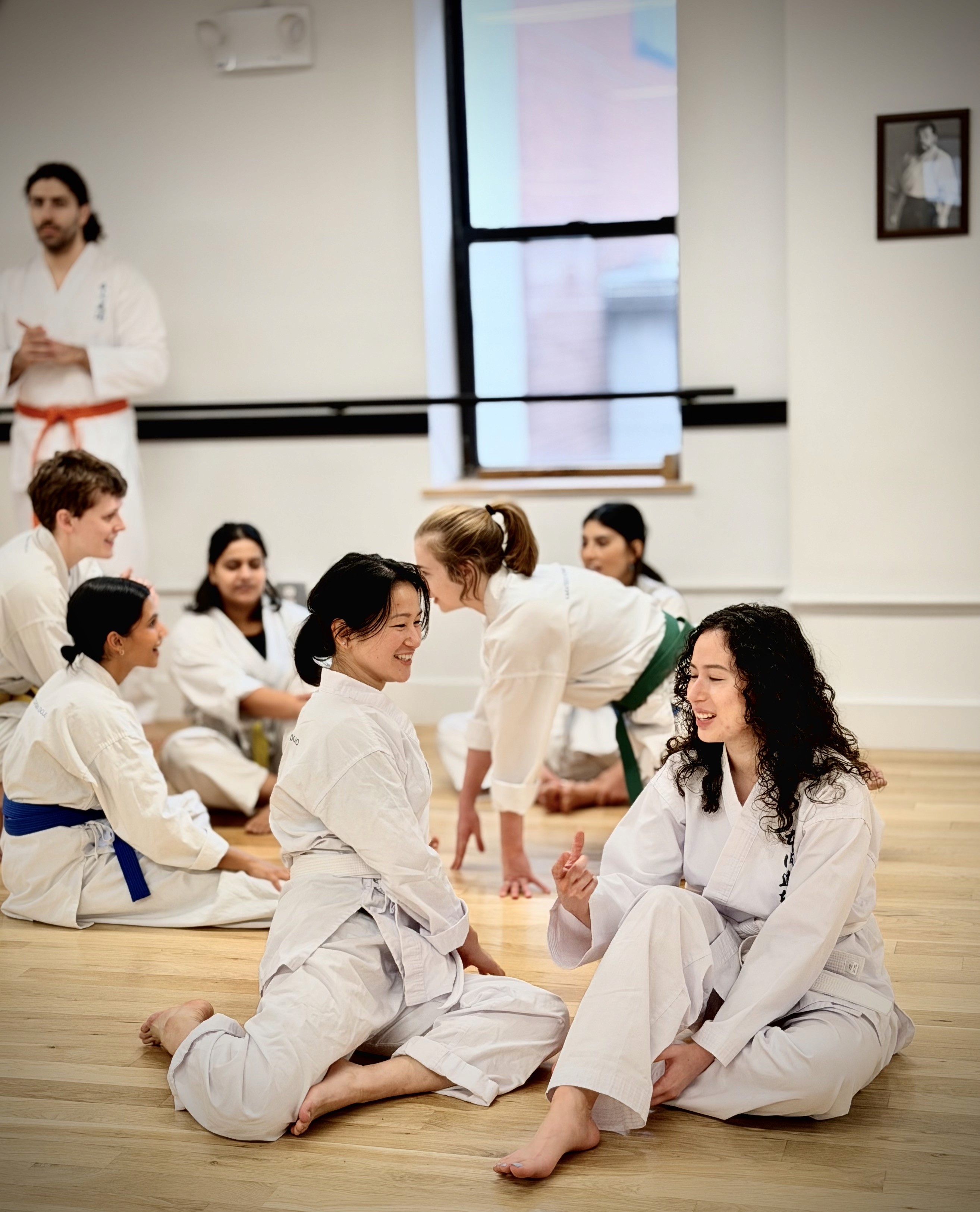 Restaurant interior with wooden tables and chairs lined against a textured wall, softly lit by round wall lamps.