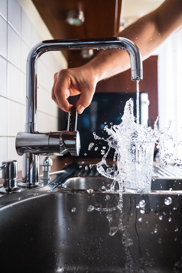 Tap with flowing water filling up a glass and splashing over the top