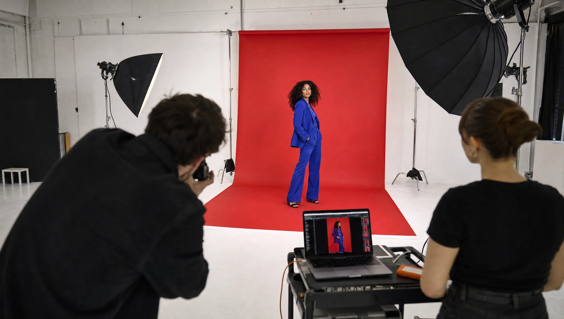Photographer shooting a model in a cobalt suit on a red paper set