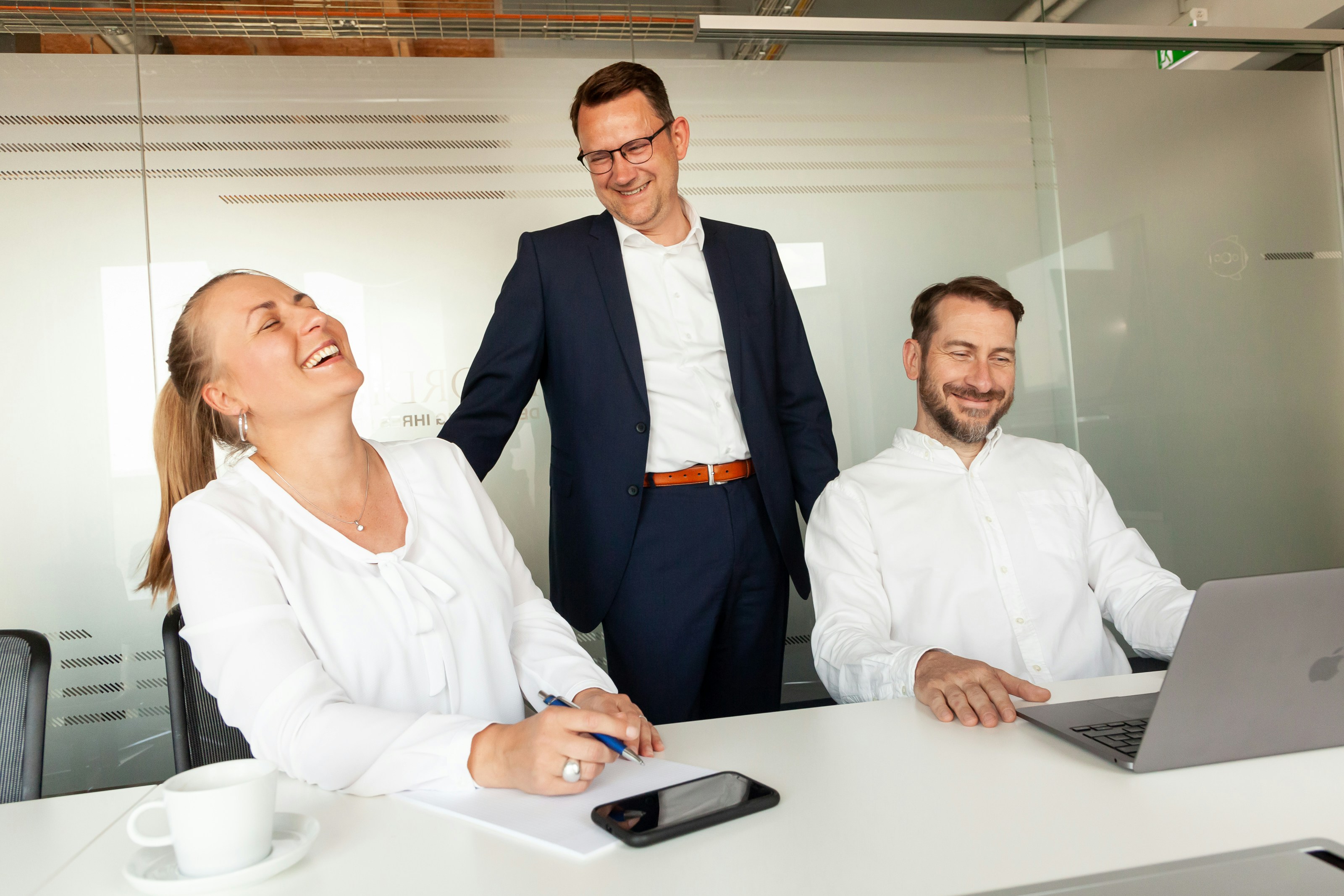 Three colleagues laughing together in an office setting.