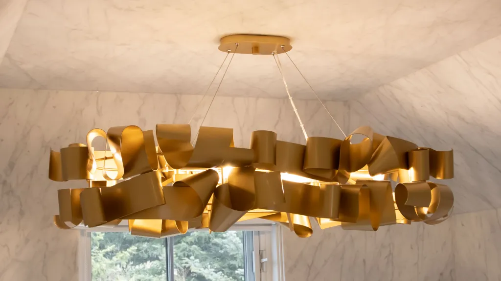 Image of Luxury gold chandelier in modern interior design with marble walls and large window. KHD Homes design-build.