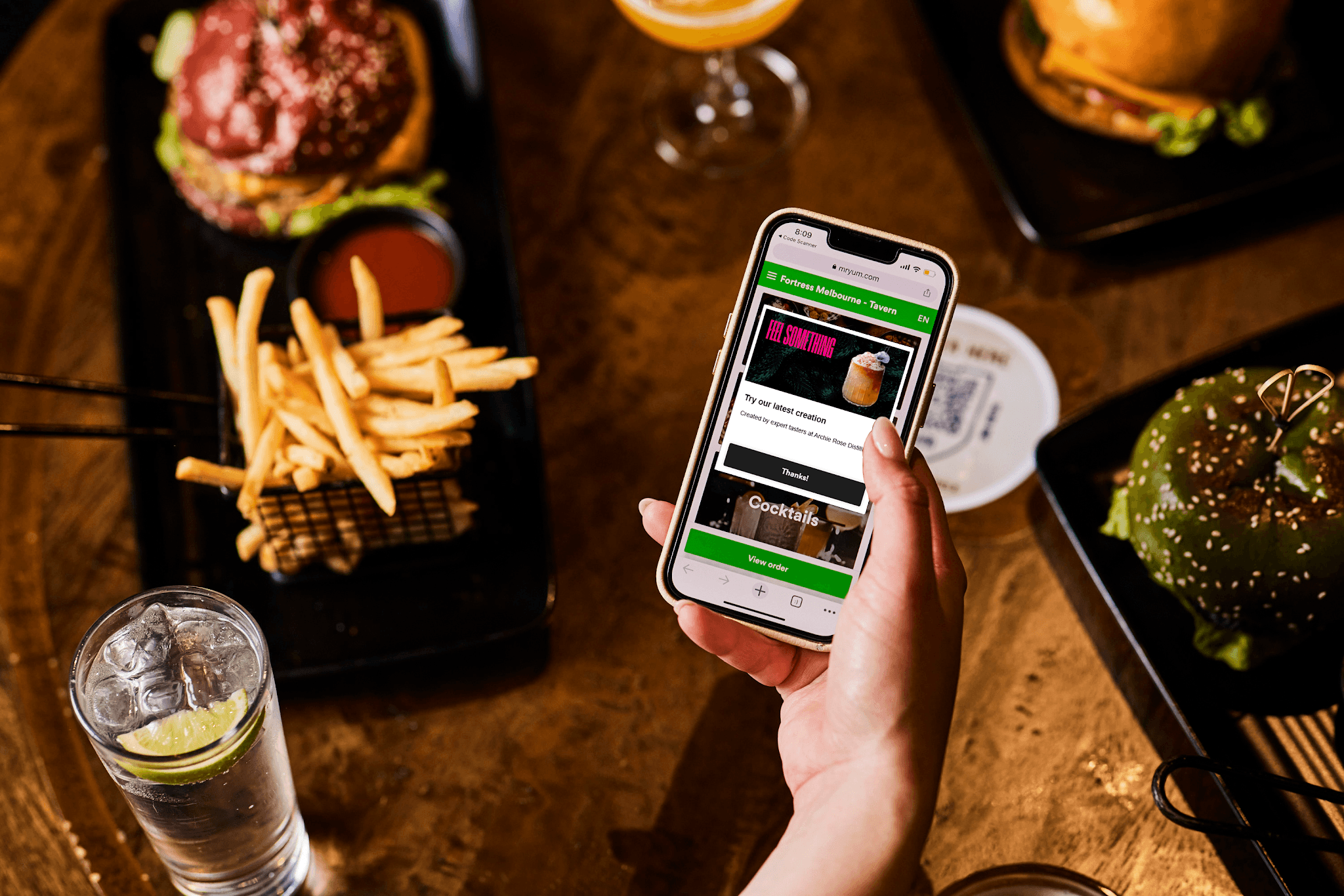A hand holding a phone above a table laden with food and drinks 