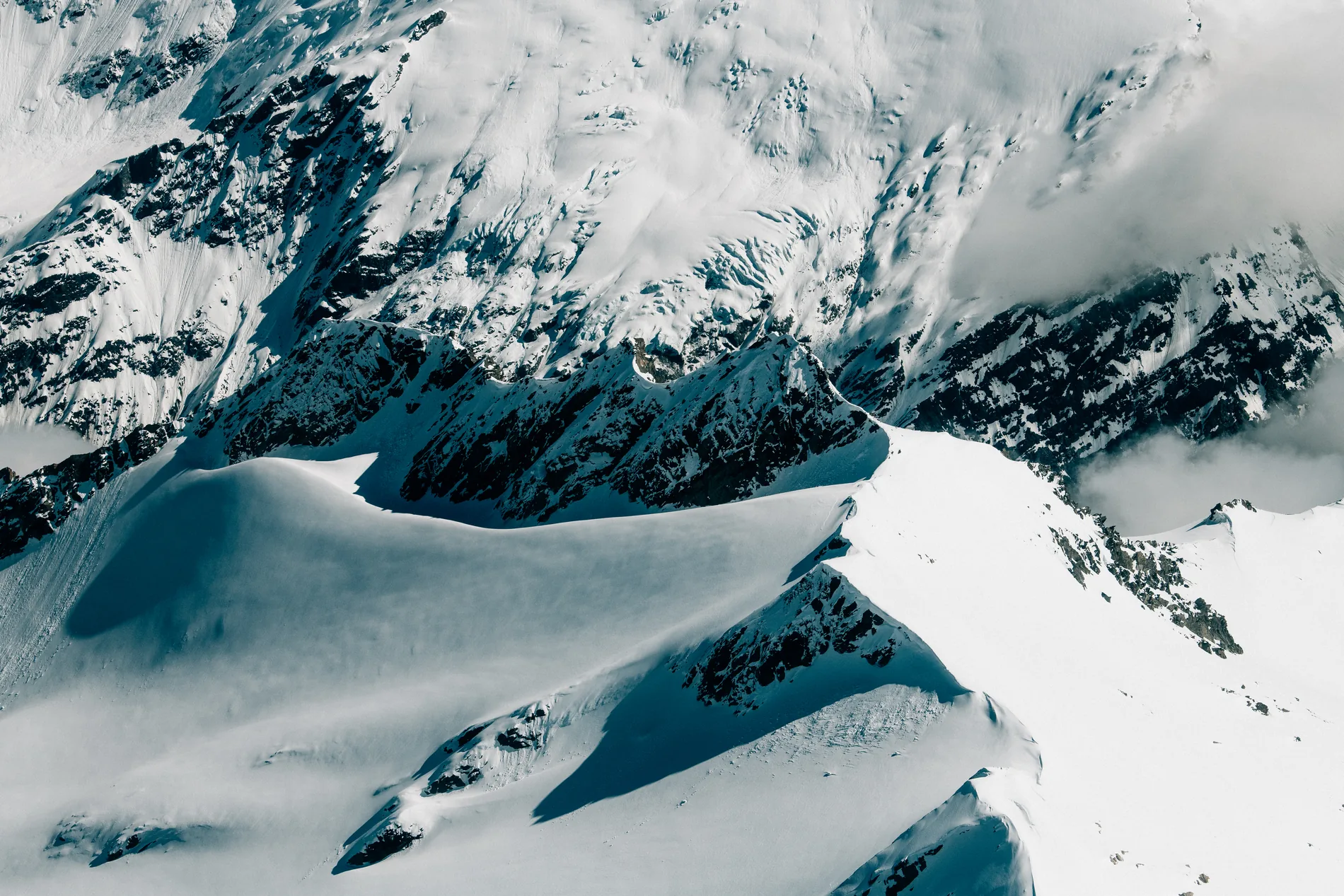 Aerial of glaciers and windblown snow curving between rocky summits