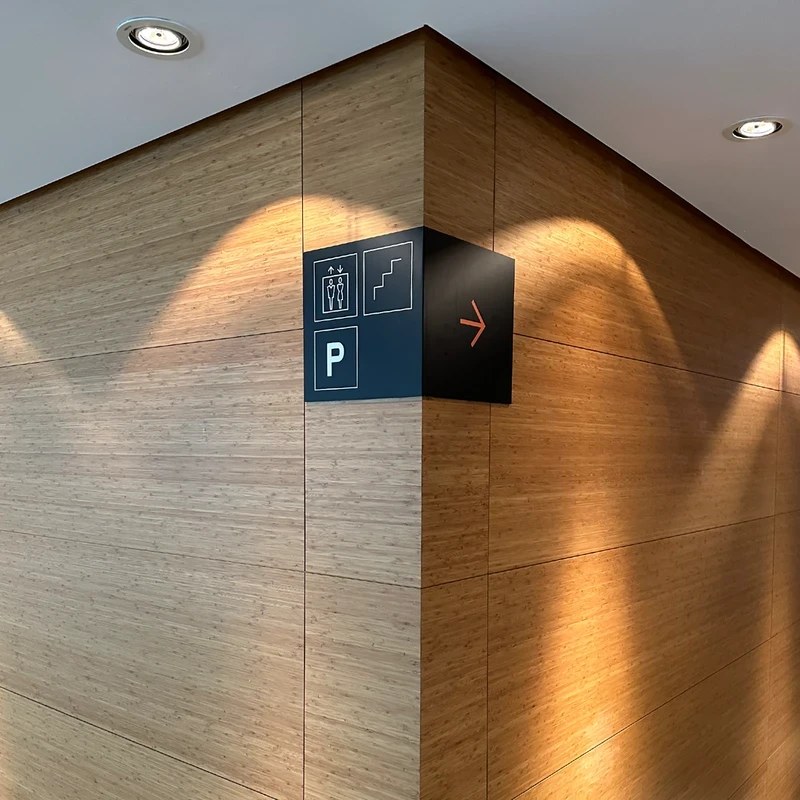 Minimalist black corner wayfinding sign on wood-grained wall