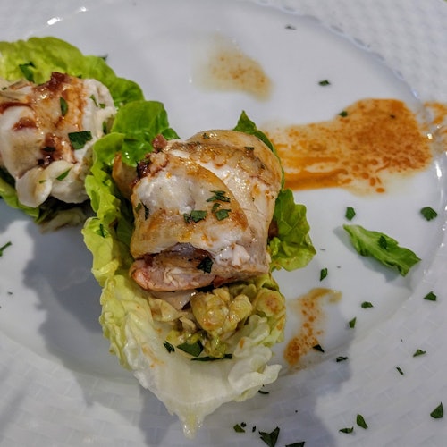 Chicken pieces on lettuce leaves, garnished with herbs and sauce, served on a white plate.